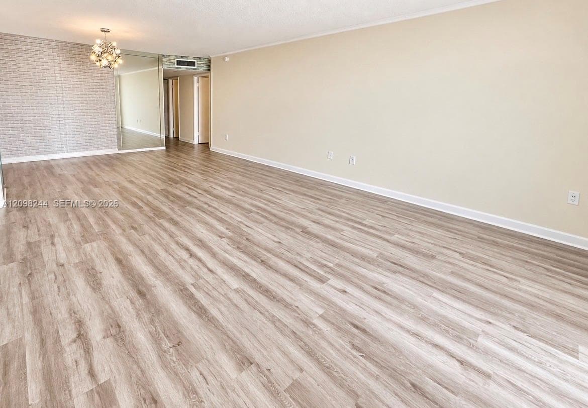 Expansive interior space featuring wood-finish flooring, a textured accent wall, mirrored wall paneling, and a multi-bulb decorative chandelier