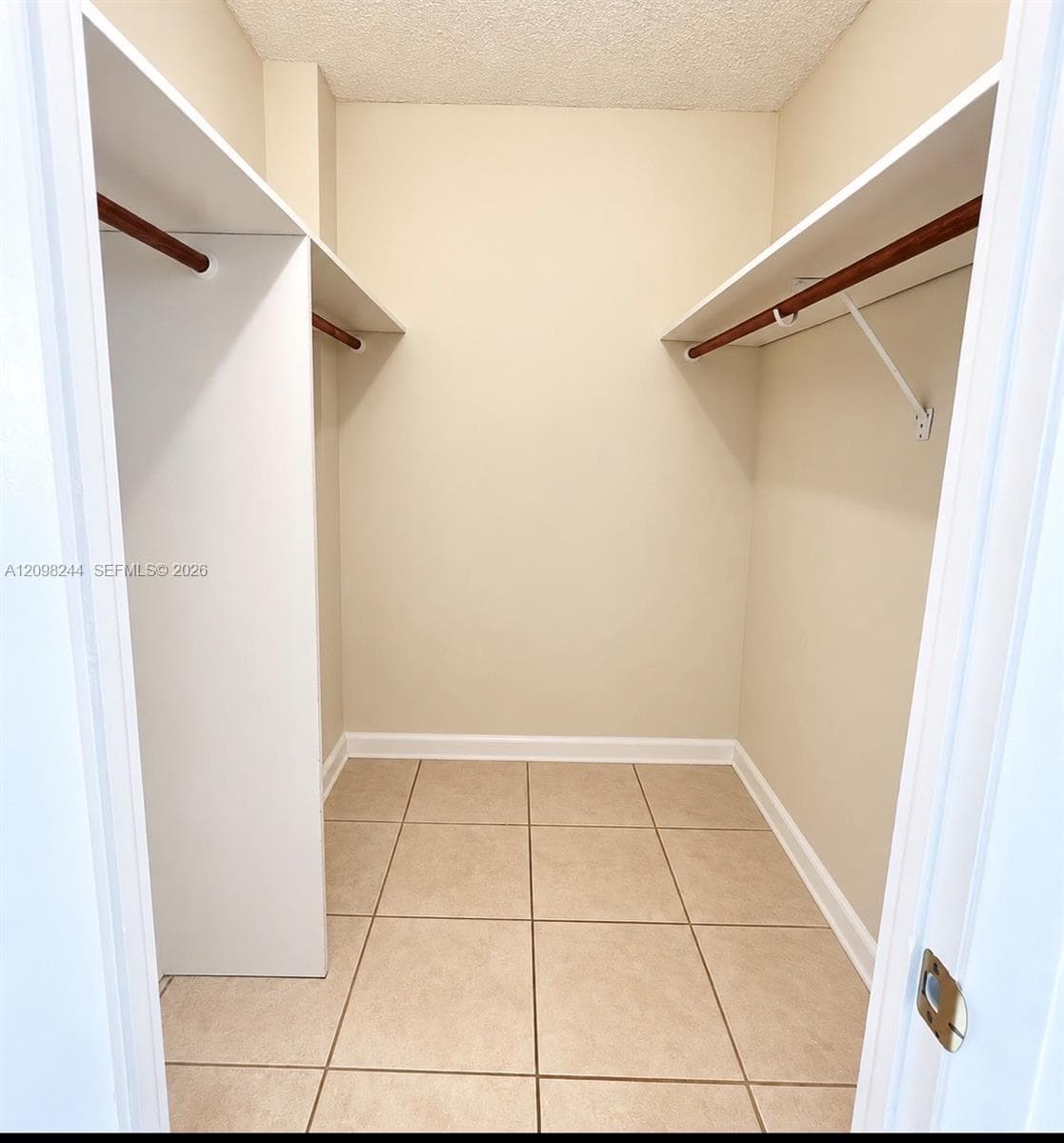 Storage closet featuring ceramic tile flooring, dual-level white shelving, and wood-finish hanging rods