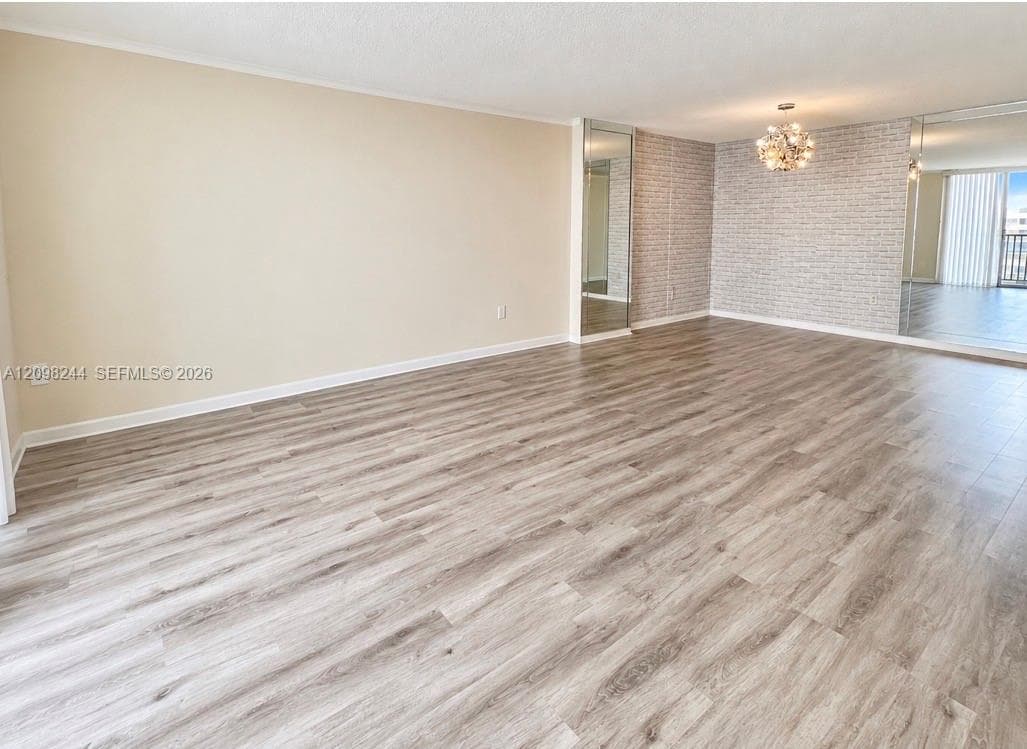 Open-concept interior featuring wood-finish flooring, a decorative textured feature wall, wall-to-wall mirrored panels, and a multi-bulb flush-mount chandelier