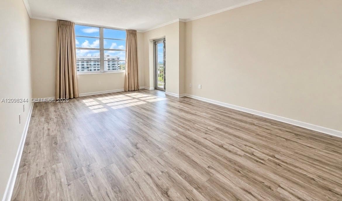 Neutral-toned interior featuring wood-finish flooring, expansive floor-to-ceiling windows, crown molding, and a glass-paneled door