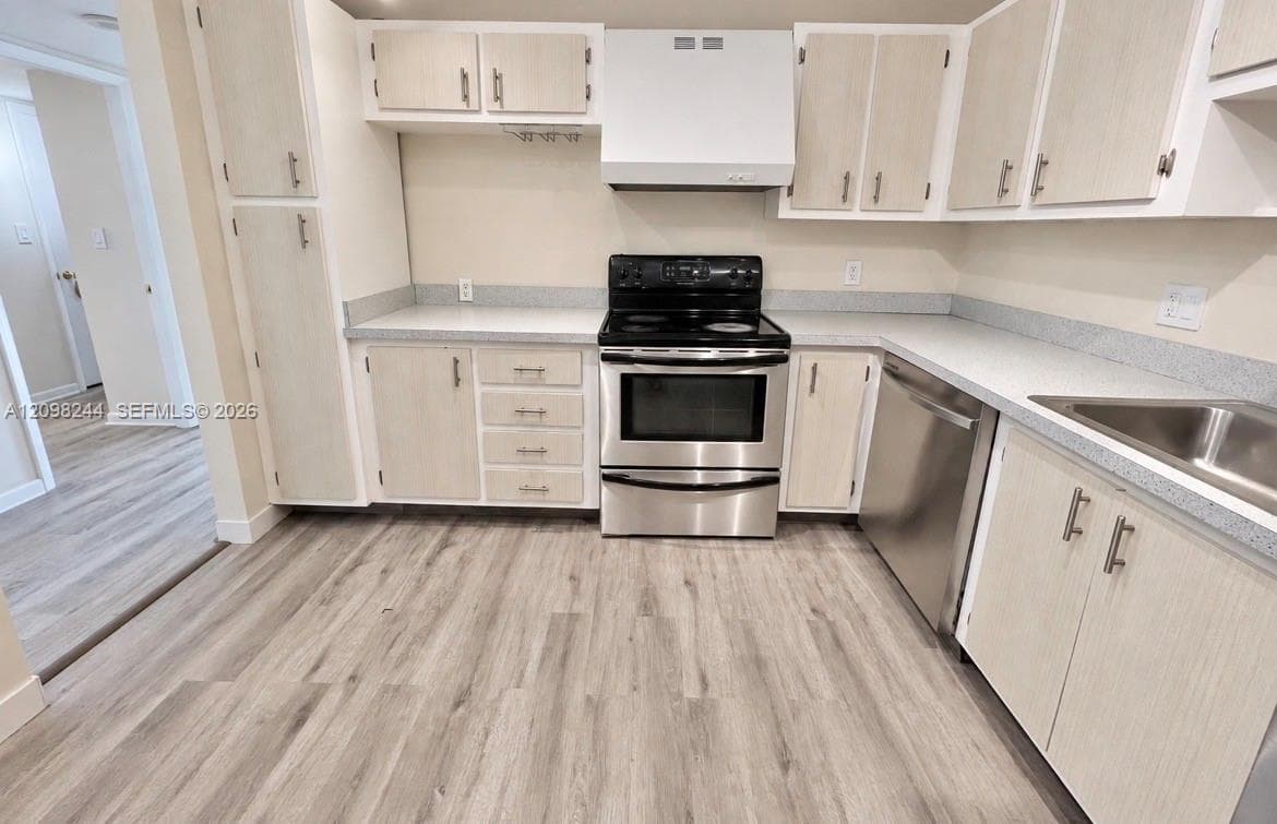 Kitchen featuring light-finish cabinetry, neutral solid-surface countertops, stainless steel appliances, and wood-finish flooring