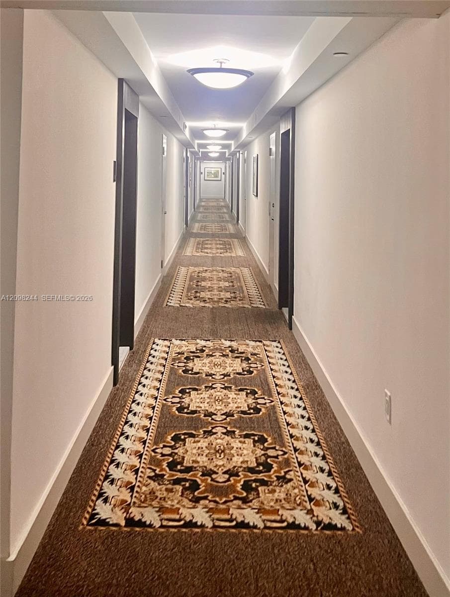 Hallway featuring recessed ceiling lighting, wall-mounted flush-mount light fixtures, and patterned carpet flooring