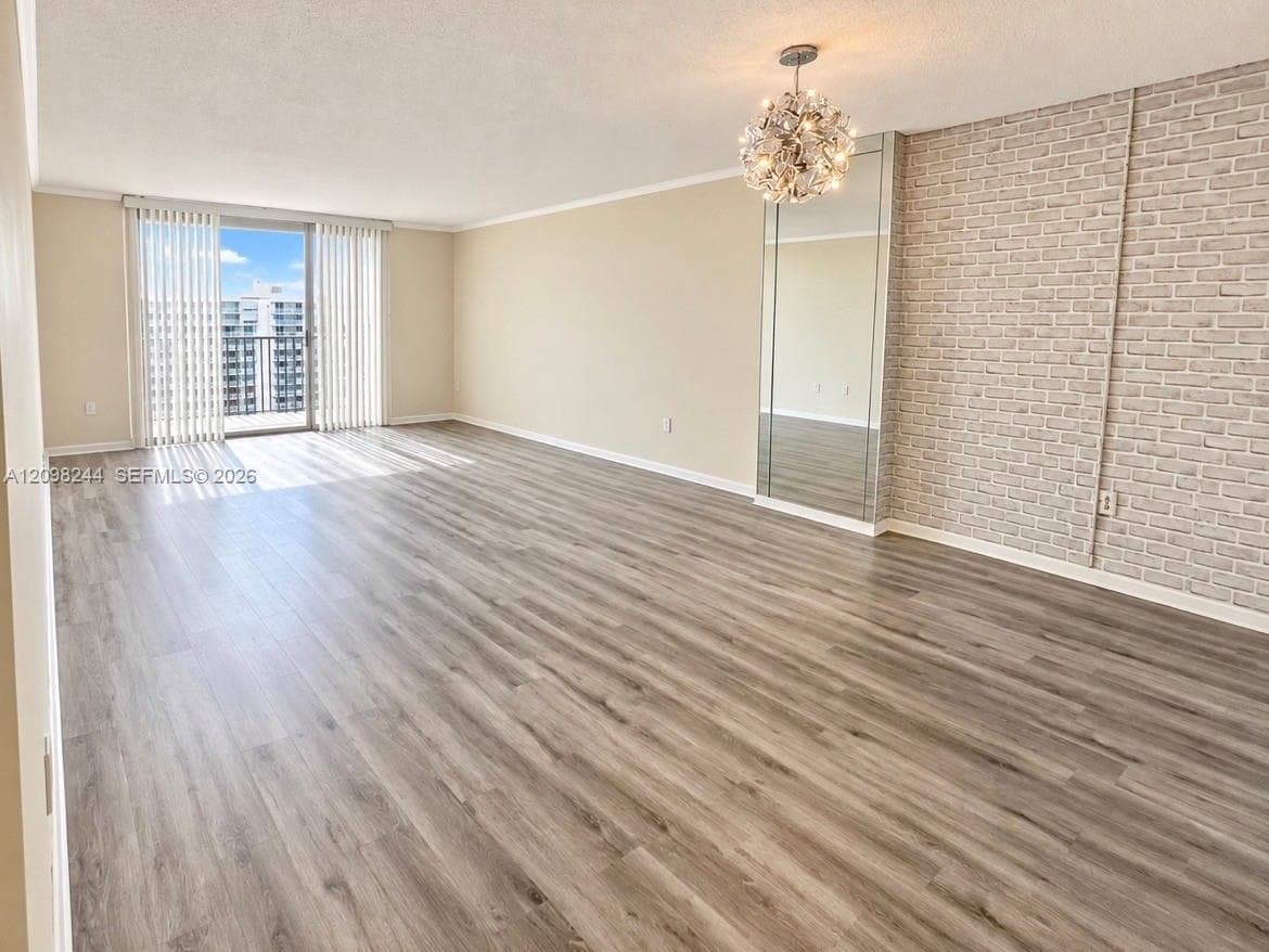 Open-concept living space featuring wood-finish flooring, a textured brick accent wall, mirrored wall paneling, a modern chandelier, and sliding glass doors