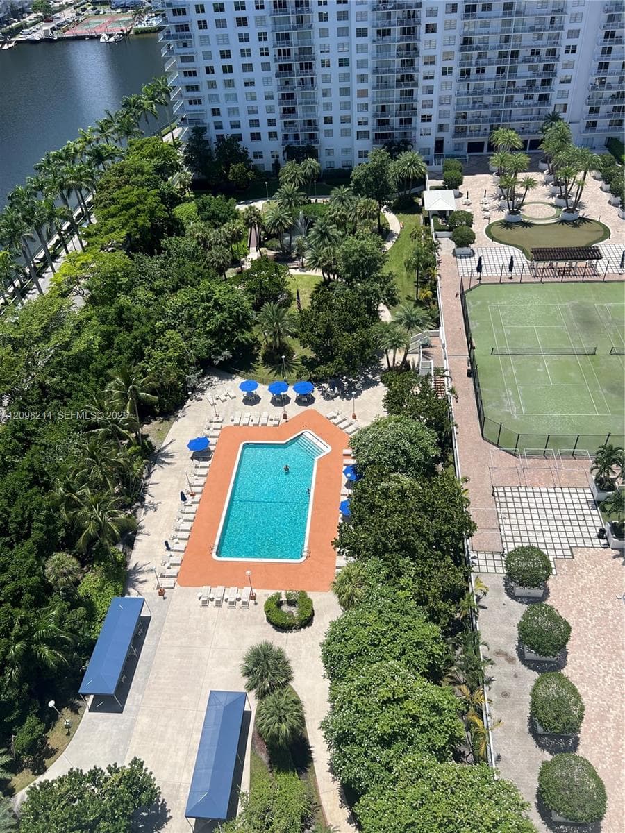 Community recreation area featuring a swimming pool, tennis court, manicured green space, and mature trees