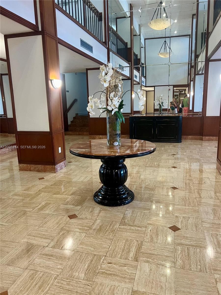 Grand foyer featuring high-gloss stone tile flooring with decorative inlay, two-story ceiling height, full-height wall mirrors, and wood-paneled columns