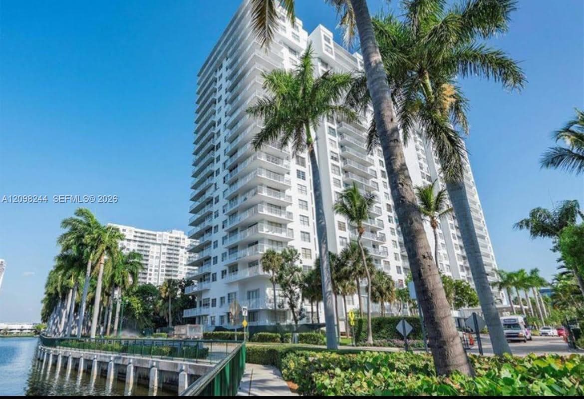 High-rise residential exterior featuring stacked private balconies, glass railings, white concrete facade, and mature palm tree landscaping