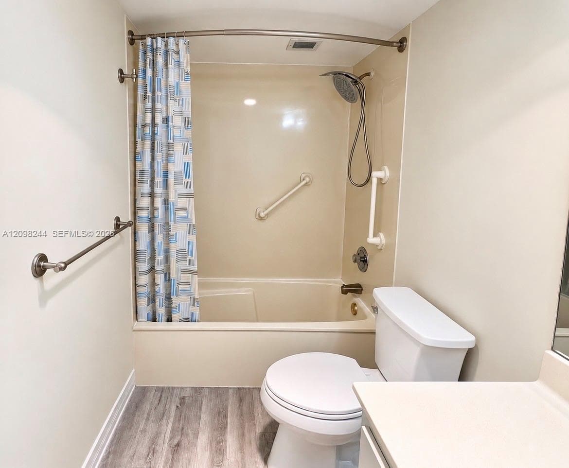 Bathroom featuring wood-finish flooring, a combination tub and shower enclosure with a handheld spray fixture, and neutral wall-mounted grab bars