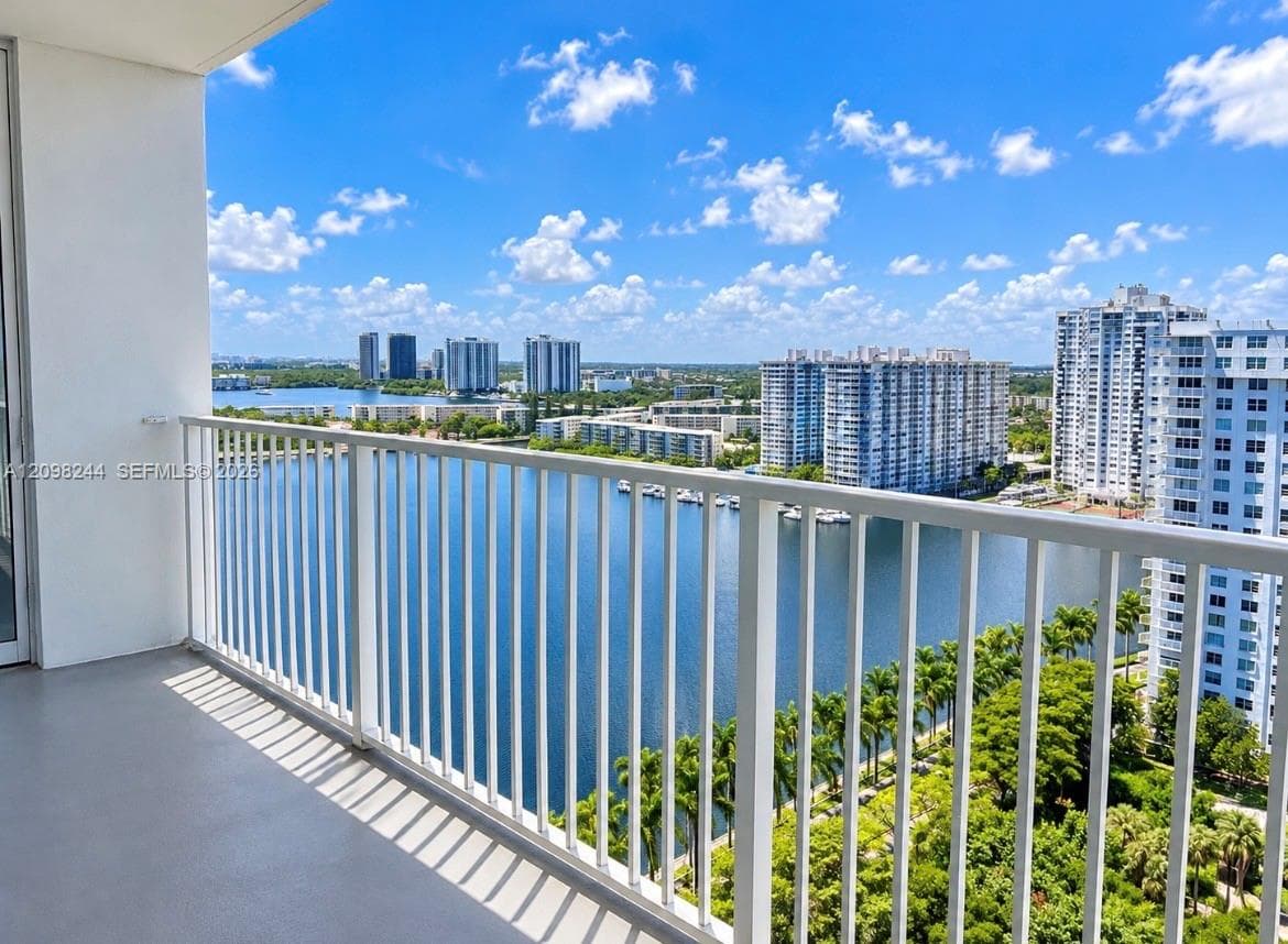 Covered balcony featuring white vertical railings, concrete flooring, and an expanse overlooking a waterfront and high-rise skyline