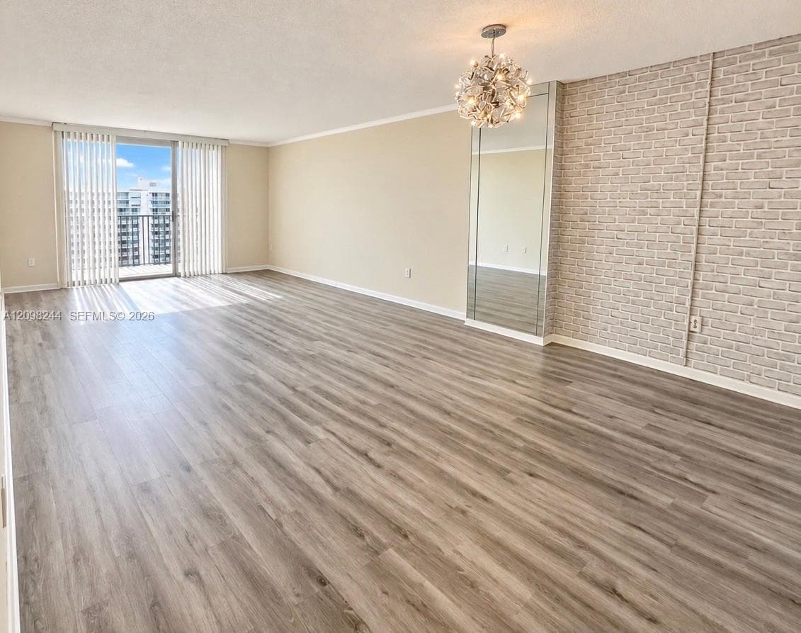 Expansive interior space featuring wood-finish flooring, a textured brick-patterned accent wall, a floor-to-ceiling mirrored panel, a tiered multi-light chandelier, and floor-to-ceiling sliding glass doors