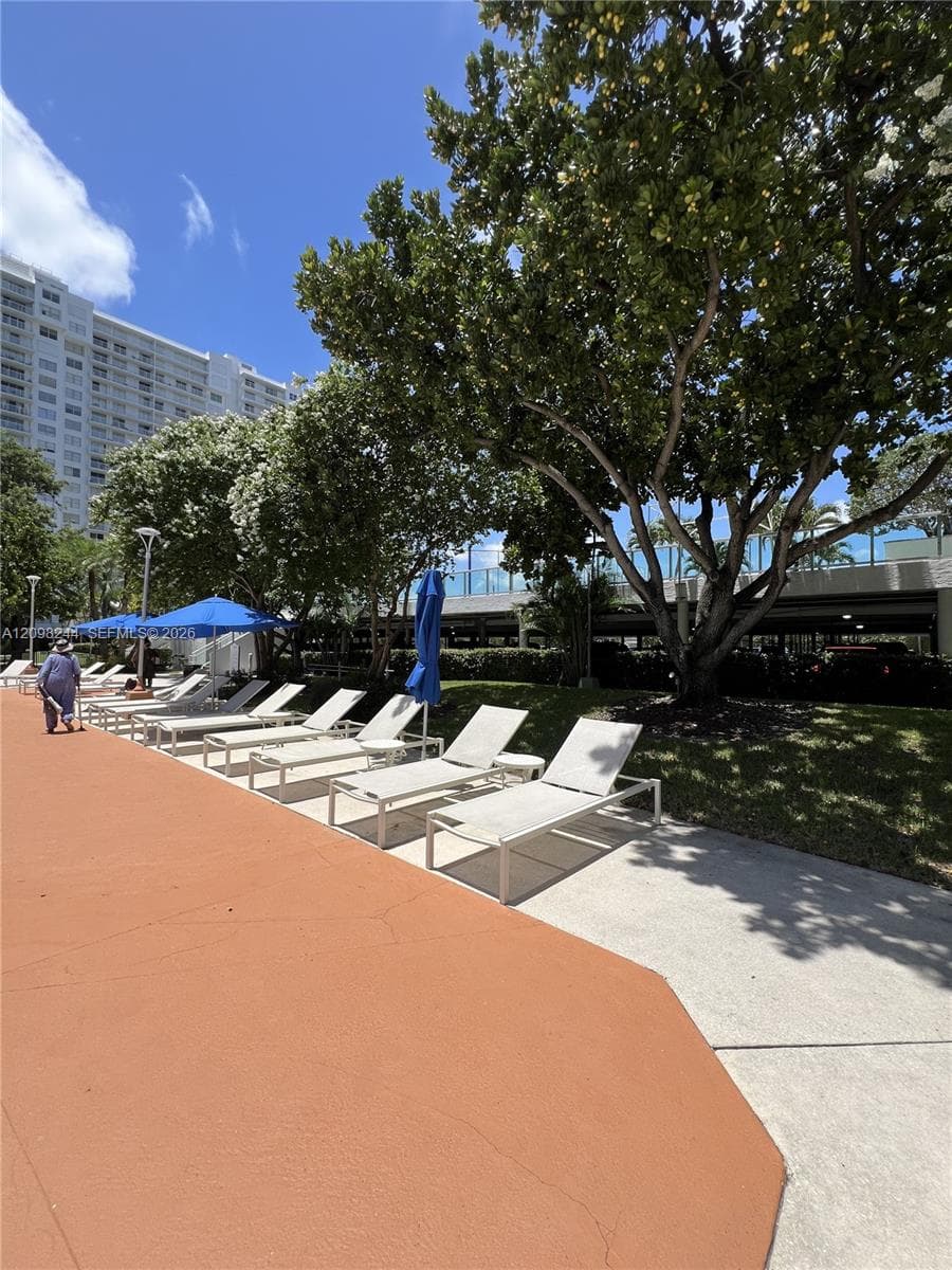 Outdoor pool deck featuring expansive concrete surfacing, mature landscaping, and multi-level parking structure