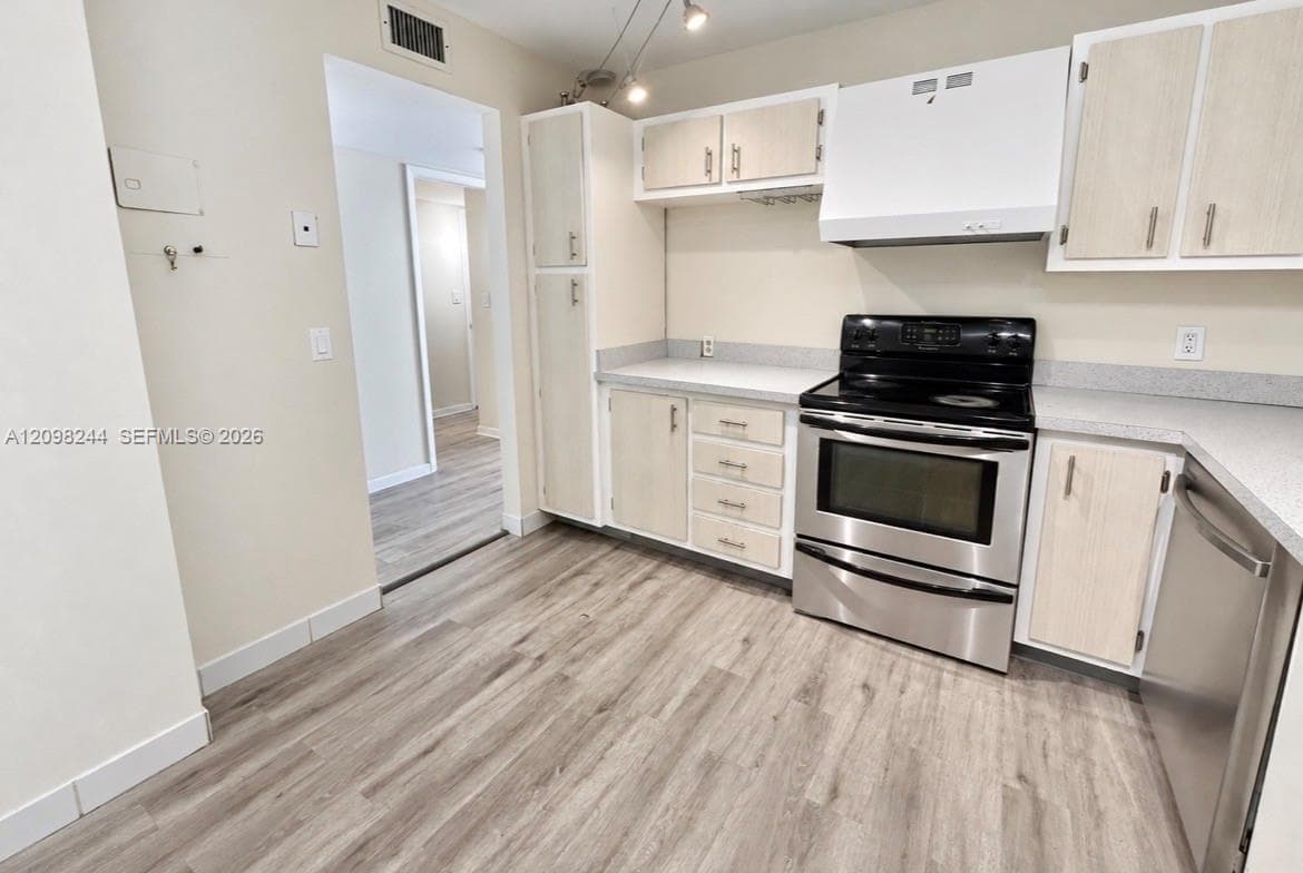 Kitchen featuring light-toned cabinetry, solid surface countertops, stainless steel appliances, and wood-finish flooring