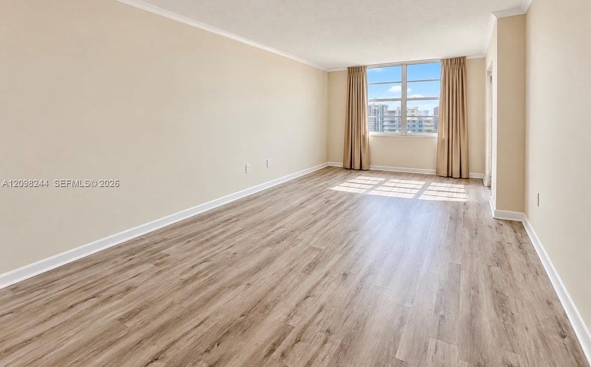 Spacious room featuring wood-finish flooring, neutral wall paint, and a large multi-pane window