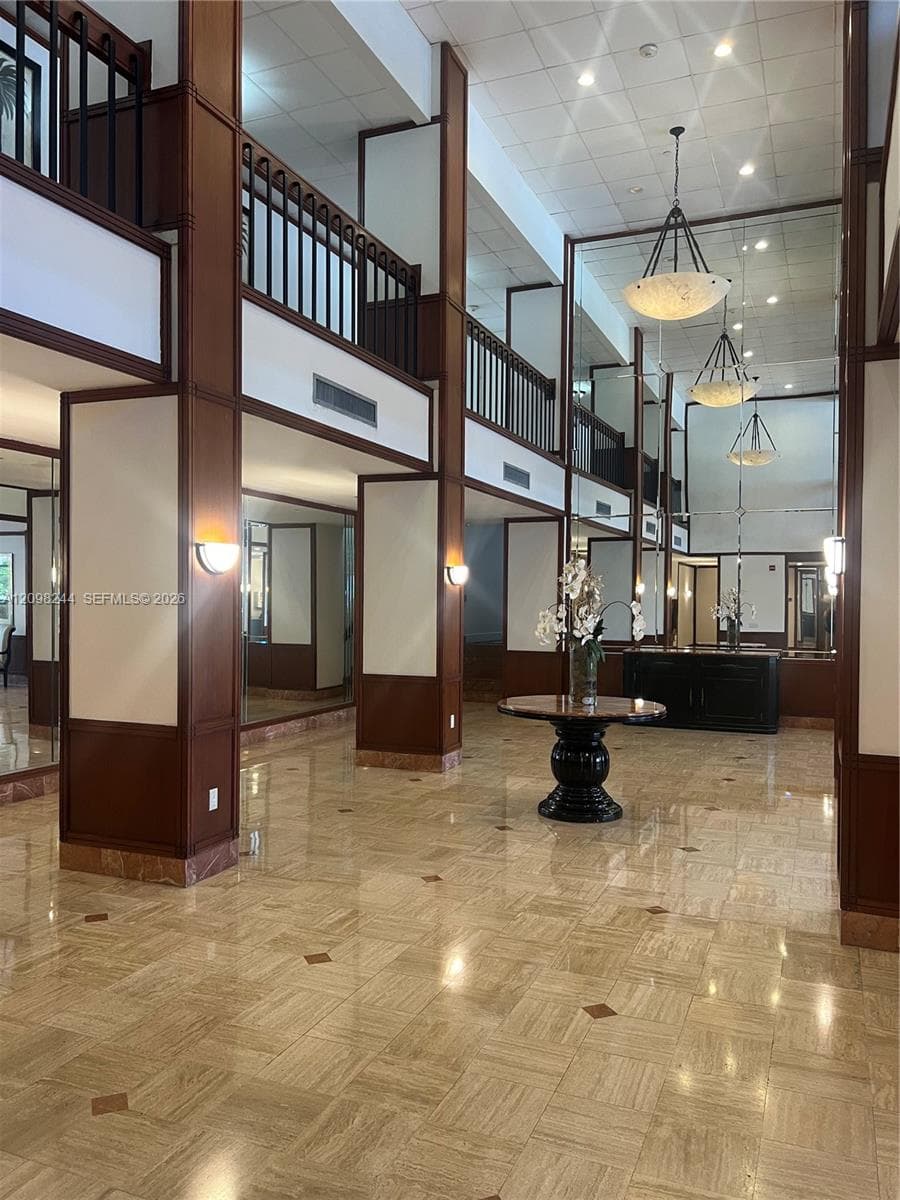 Double-height foyer featuring polished stone flooring with decorative inlays, expansive wall mirrors, dark wood-finished paneling, black metal railings, and three tiered pendant light fixtures