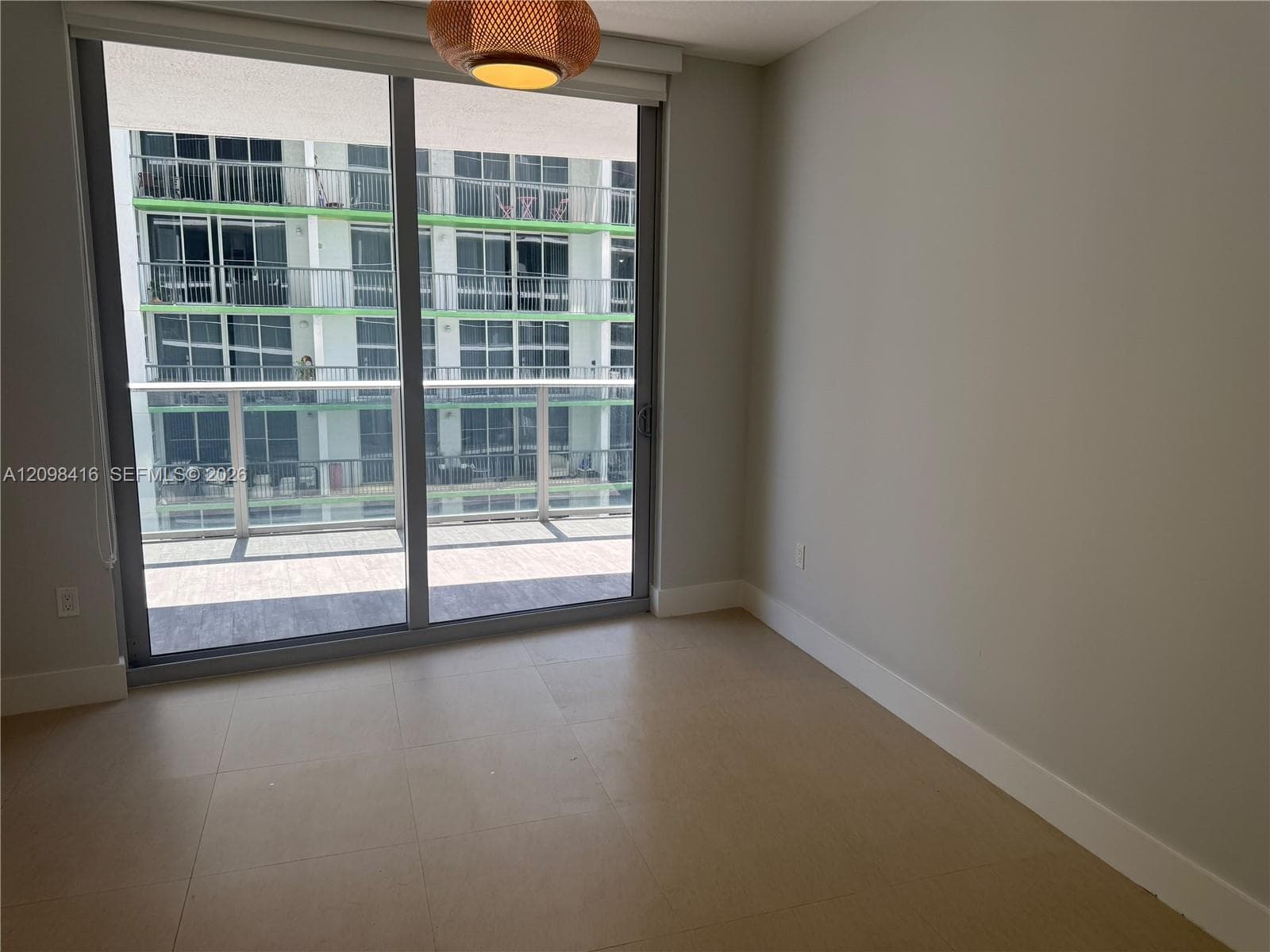 Sliding glass doors opening to an outdoor balcony with glass railings, neutral tone walls, and large format tile flooring