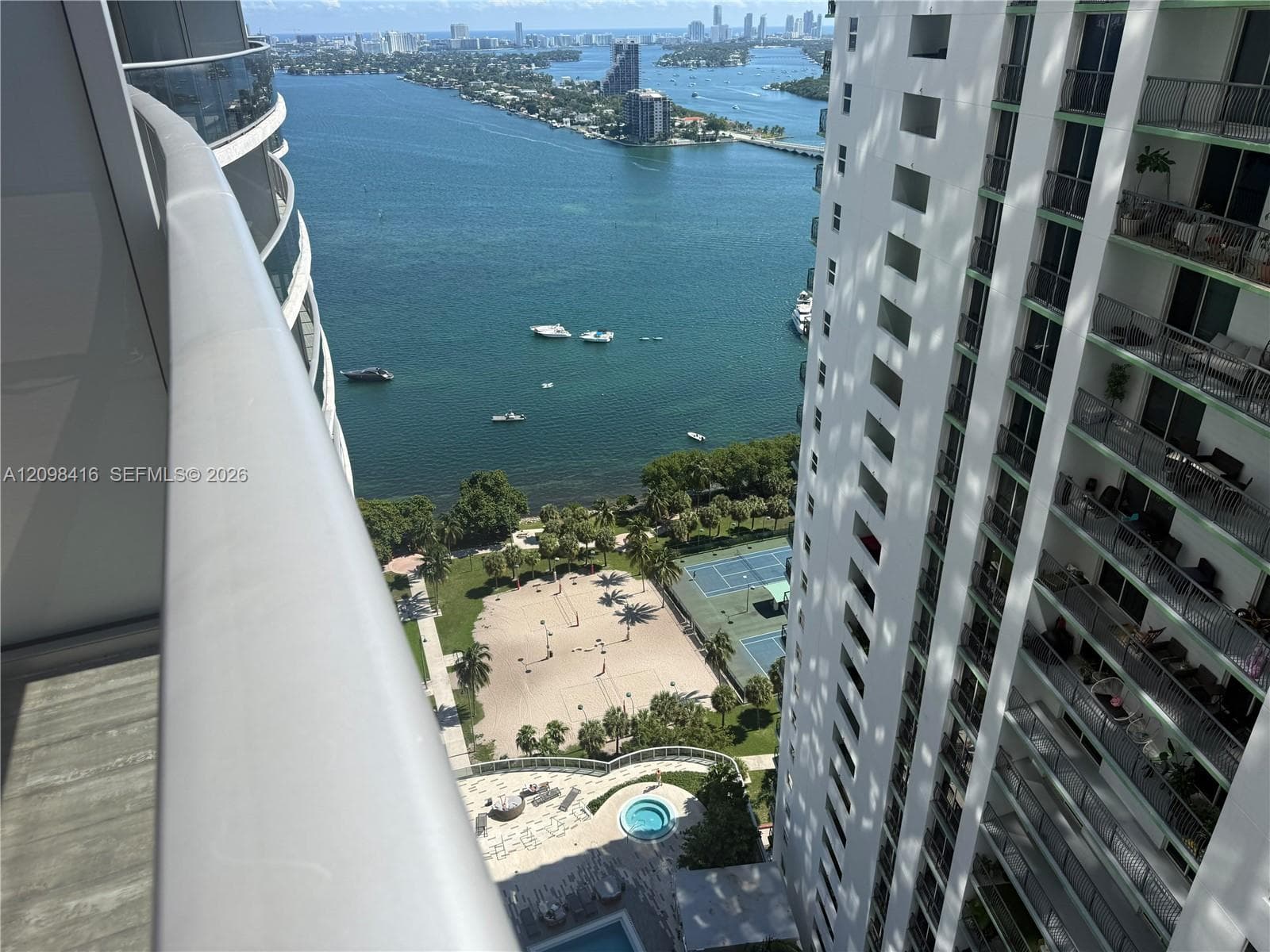 Expansive water body, multiple watercraft, sandy recreation area, tennis courts, and a circular pool feature