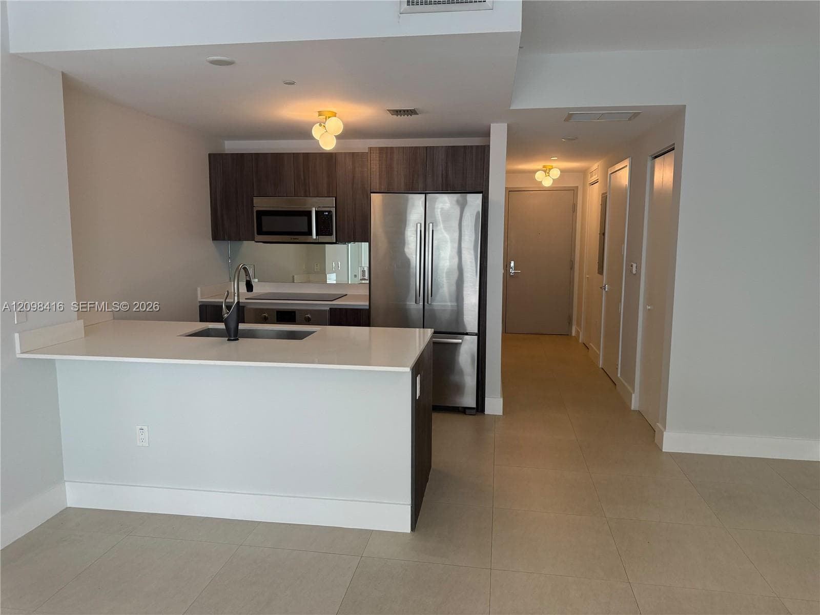 Kitchen featuring wood-finish cabinetry, stainless steel appliances, a white countertop island, and tile flooring