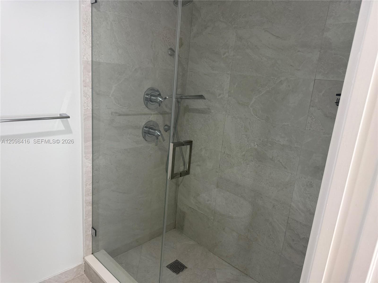 Glass-enclosed shower with a chrome towel bar, floor-to-ceiling tile, and chrome fixtures