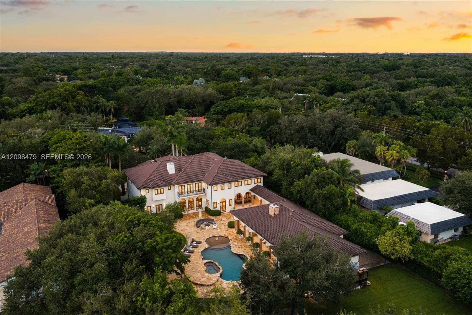 Aerial perspective of an expansive residence featuring a multi-gabled tile roof, stone-paved pool deck, custom-shaped swimming pool with integrated spa, and mature perimeter landscaping