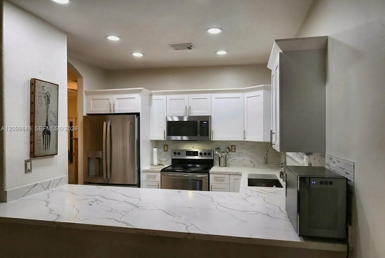 Kitchen featuring white shaker-style cabinetry, white countertops with grey veining, stainless steel appliances, recessed ceiling lighting, and a neutral tile backsplash