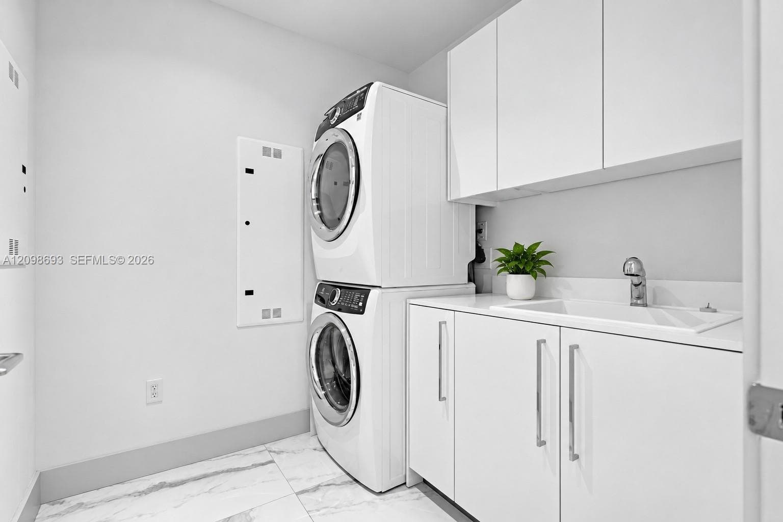 Laundry area featuring white cabinetry, a built-in sink with a chrome faucet, quartz countertop, and large-format tile flooring