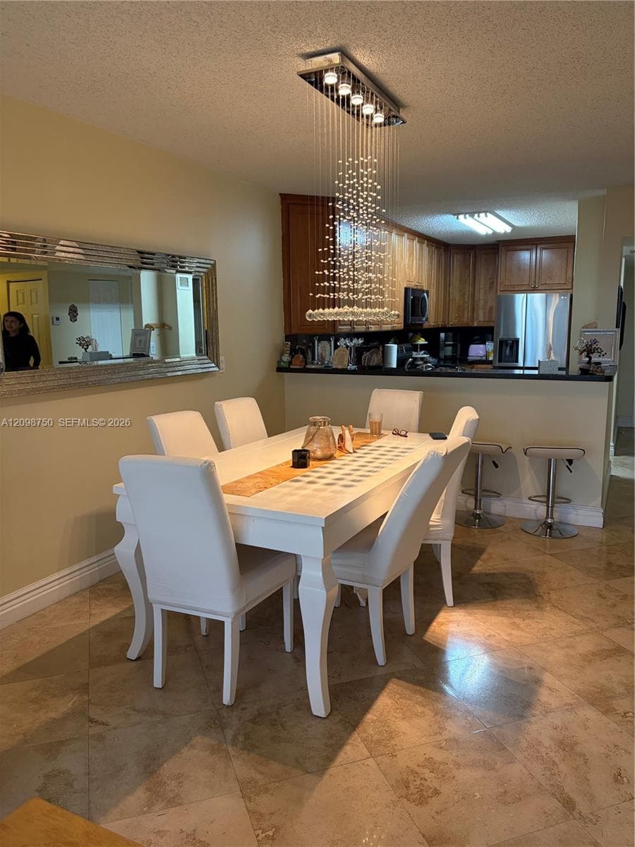 Dining area featuring large-format tile flooring, a multi-strand crystal chandelier, and a decorative wall-mounted mirror