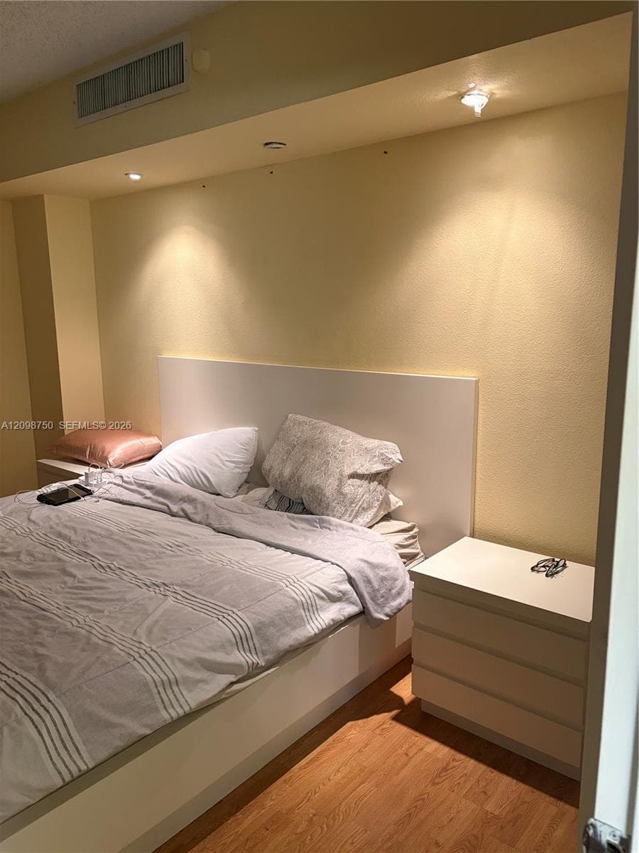 Built-in white headboard, recessed ceiling lighting, and wood-finish flooring