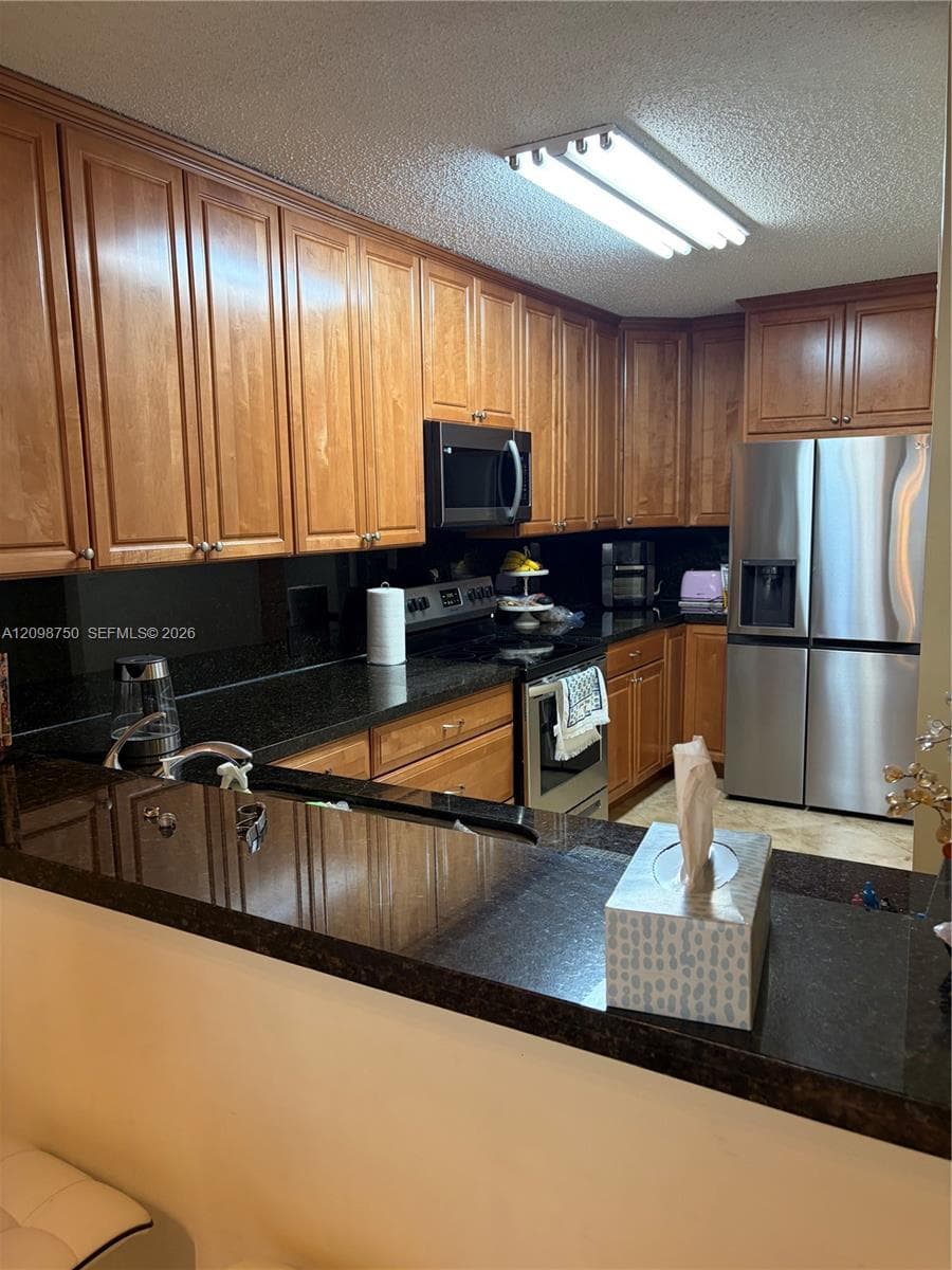 Kitchen featuring wood cabinetry, stone countertops, stainless steel appliances, a breakfast bar, and integrated lighting