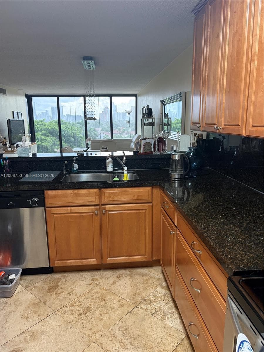 Kitchen featuring stained wood cabinetry, dark stone countertops, stainless steel dishwasher, tile flooring, and floor-to-ceiling windows