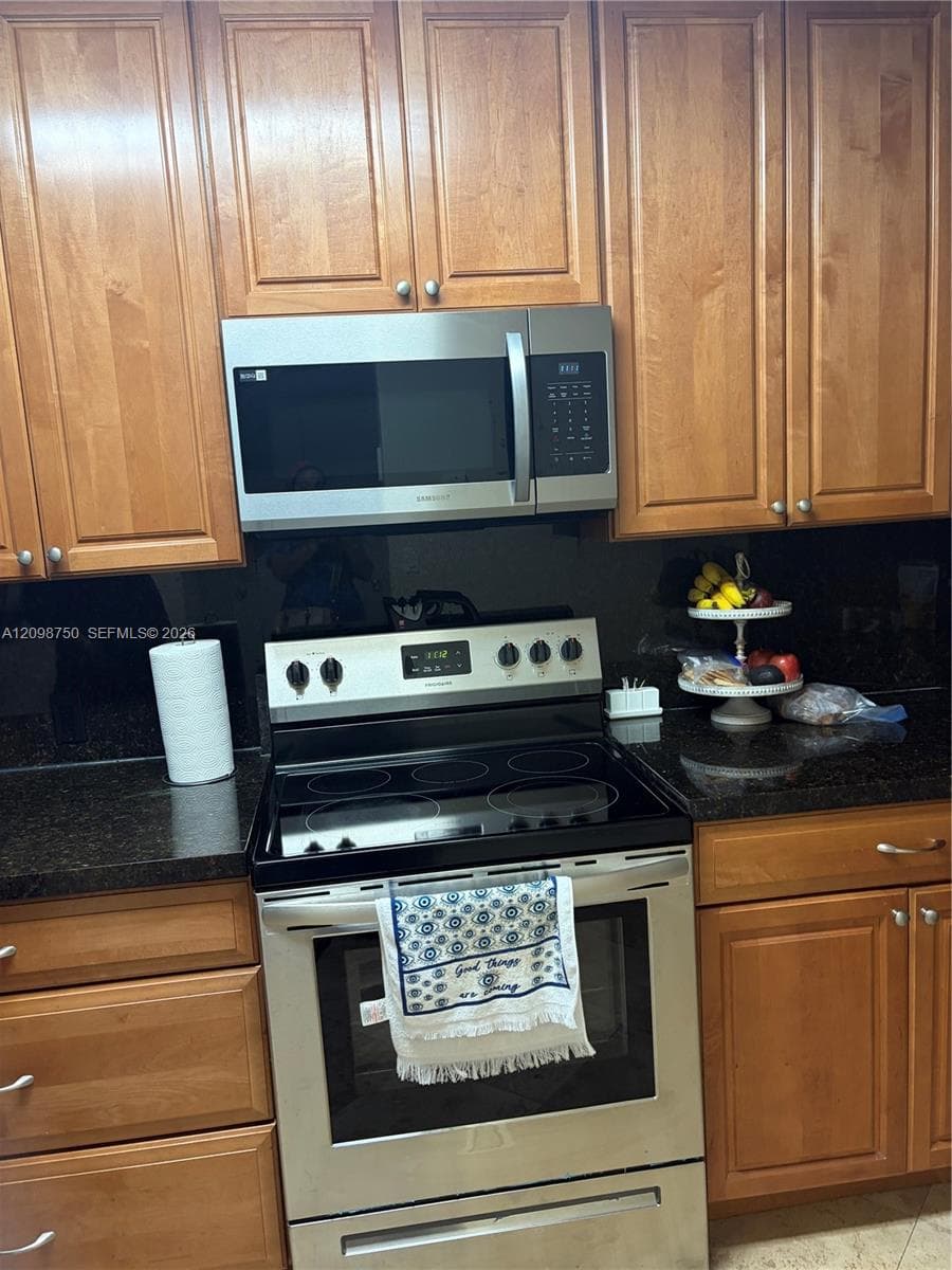 Kitchen featuring wood cabinetry, dark stone countertops, stainless steel microwave, and stainless steel electric range