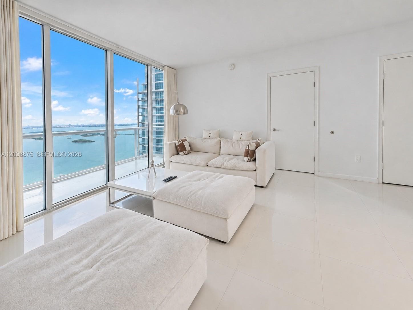 Floor-to-ceiling glass sliding doors, water scenery, modern built-in overhead lighting, and white tile flooring