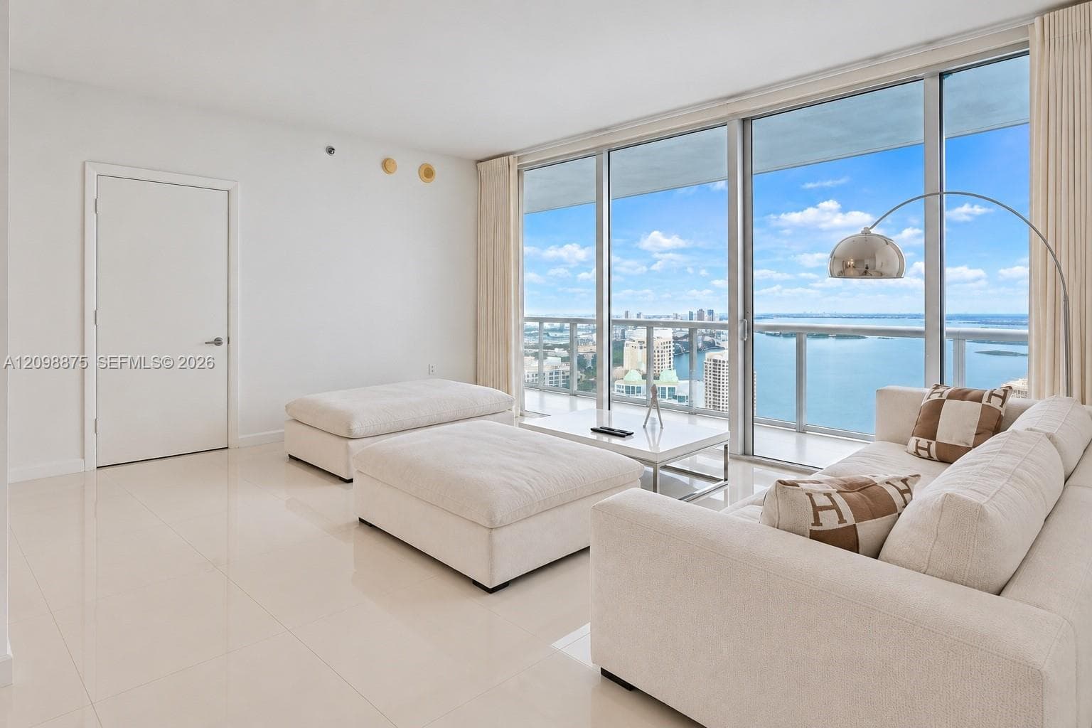 Floor-to-ceiling glass doors, expansive water and city scenery, light-toned tile flooring, and recessed ceiling lights
