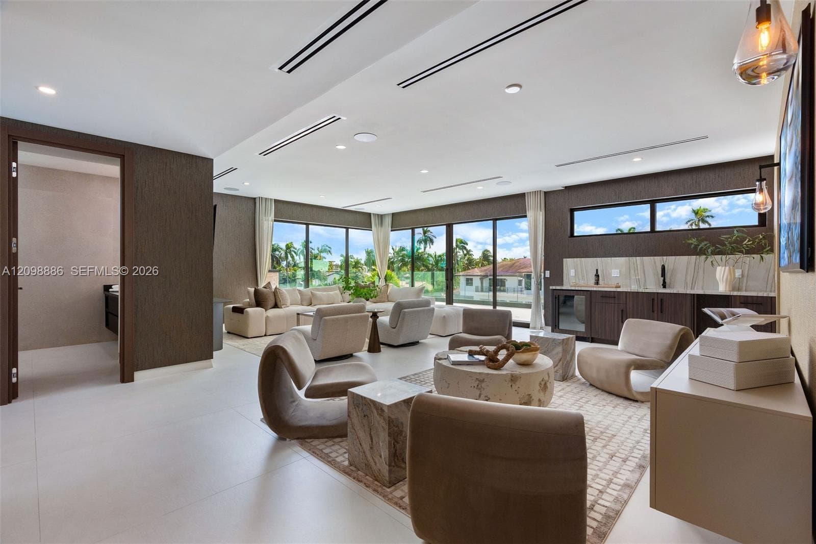 Large-format tile flooring, recessed linear lighting, floor-to-ceiling glass sliding doors, built-in wet bar with stone backsplash, and dark textured wall treatments