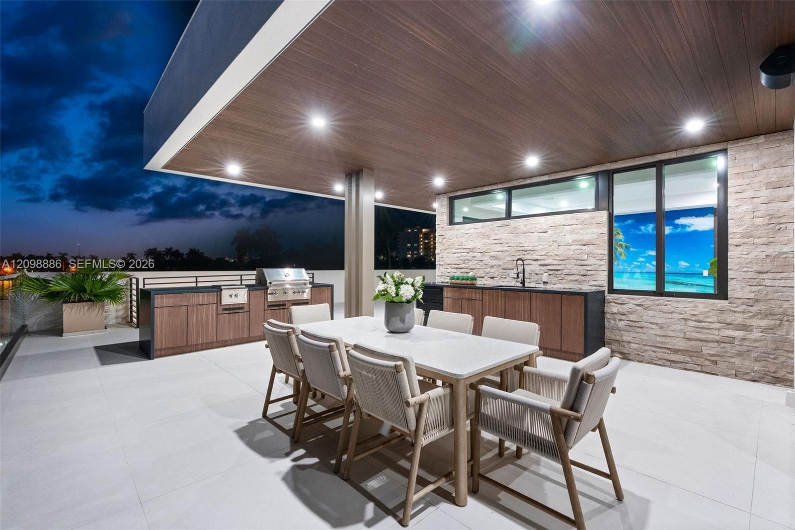 Covered outdoor terrace featuring a built-in stainless steel grill, stone veneer accent wall, recessed lighting, and expansive wood-finish ceiling soffits