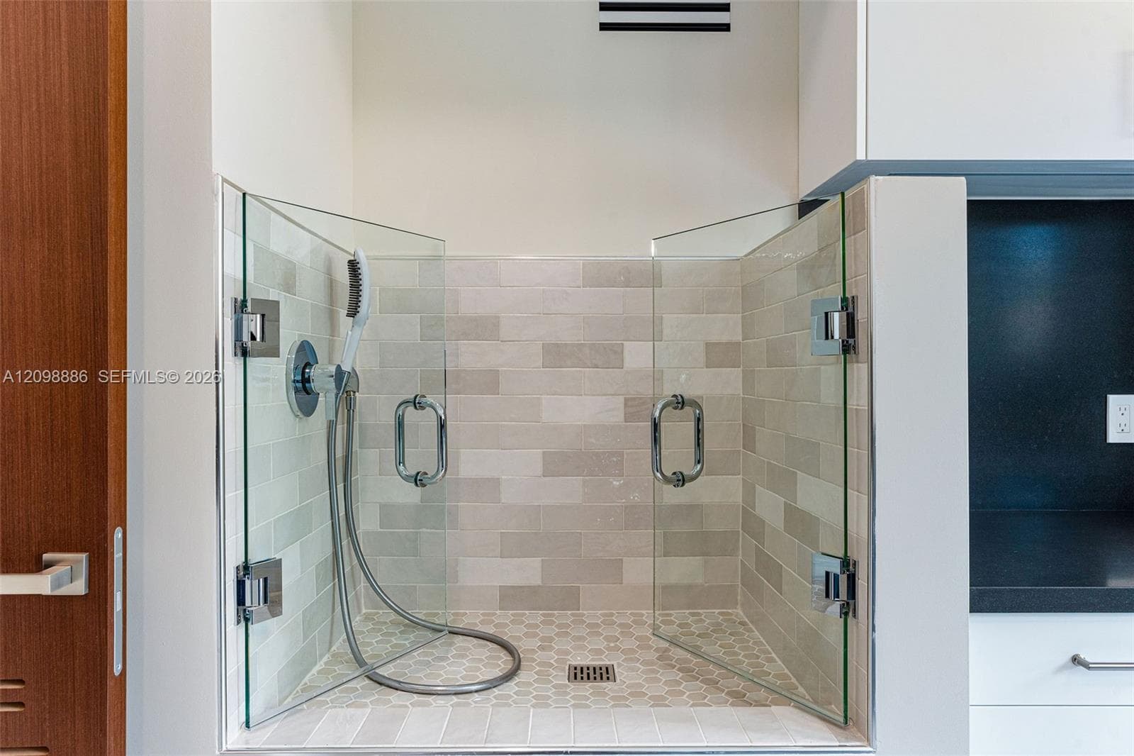 Glass-enclosed station featuring a handheld shower fixture, subway-tile wall surround, hexagonal floor tile, and polished chrome hardware