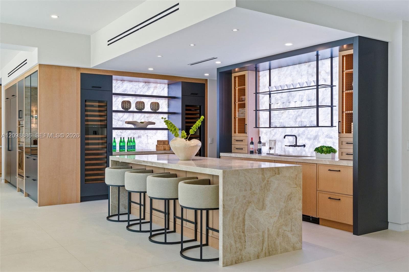 Kitchen featuring a waterfall-edge stone island, built-in dual wine refrigeration, stone slab backsplash, recessed ceiling lighting, and custom cabinetry with open metal shelving