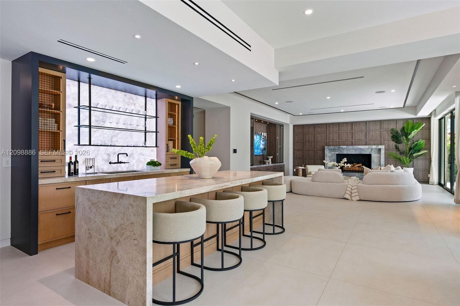 Stone-topped kitchen island with bar seating, custom cabinetry featuring integrated shelving, recessed lighting, and floor-to-ceiling wood wall paneling with an inset fireplace