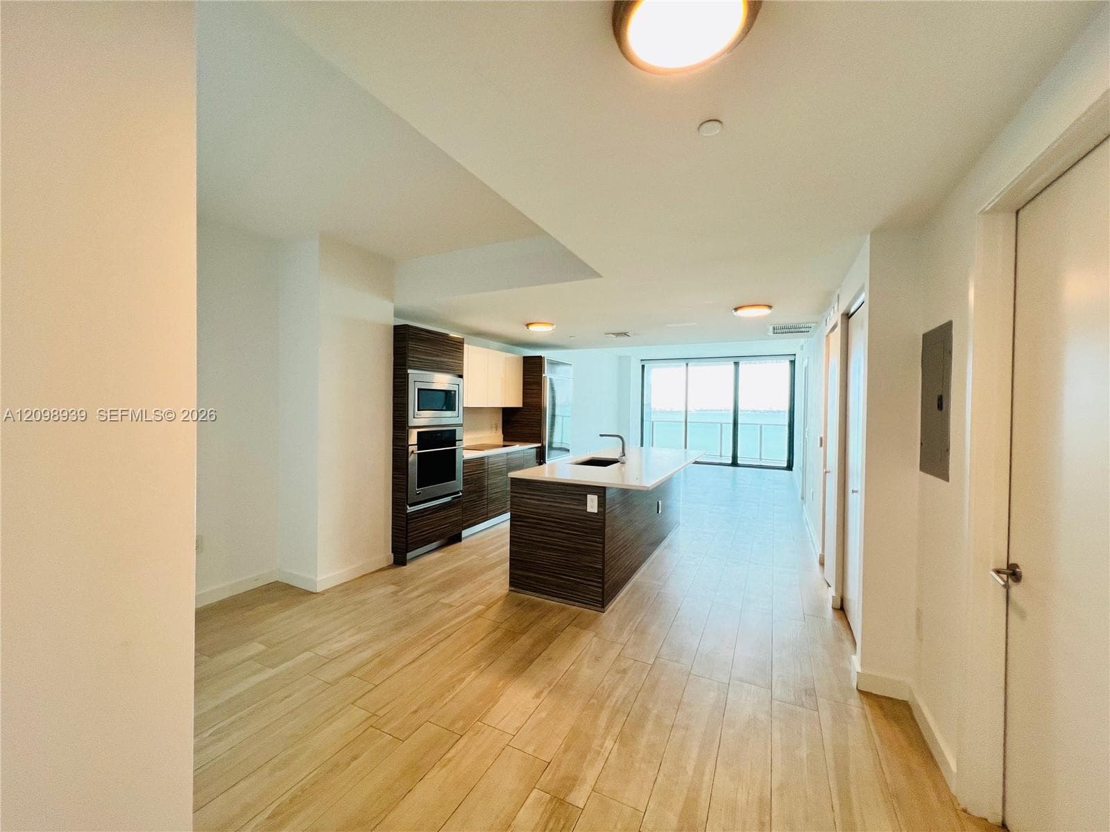Open-concept floor plan featuring wood-finish flooring, a kitchen island with integrated sink, stainless steel built-in appliances, and expansive sliding glass doors