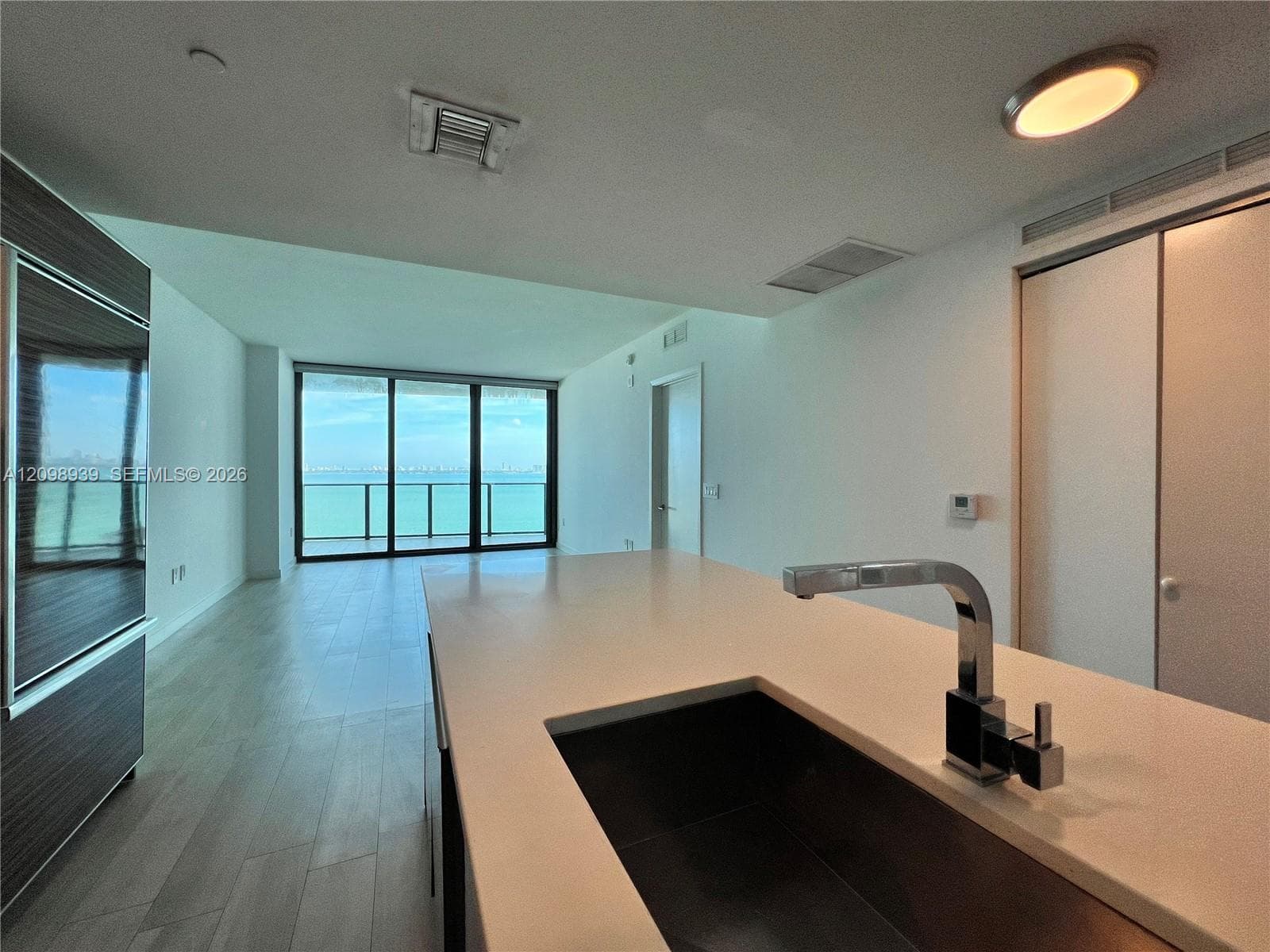 Expansive floor-to-ceiling windows, water expanse backdrop, island with integrated sink, contemporary faucet, and wood-finish flooring