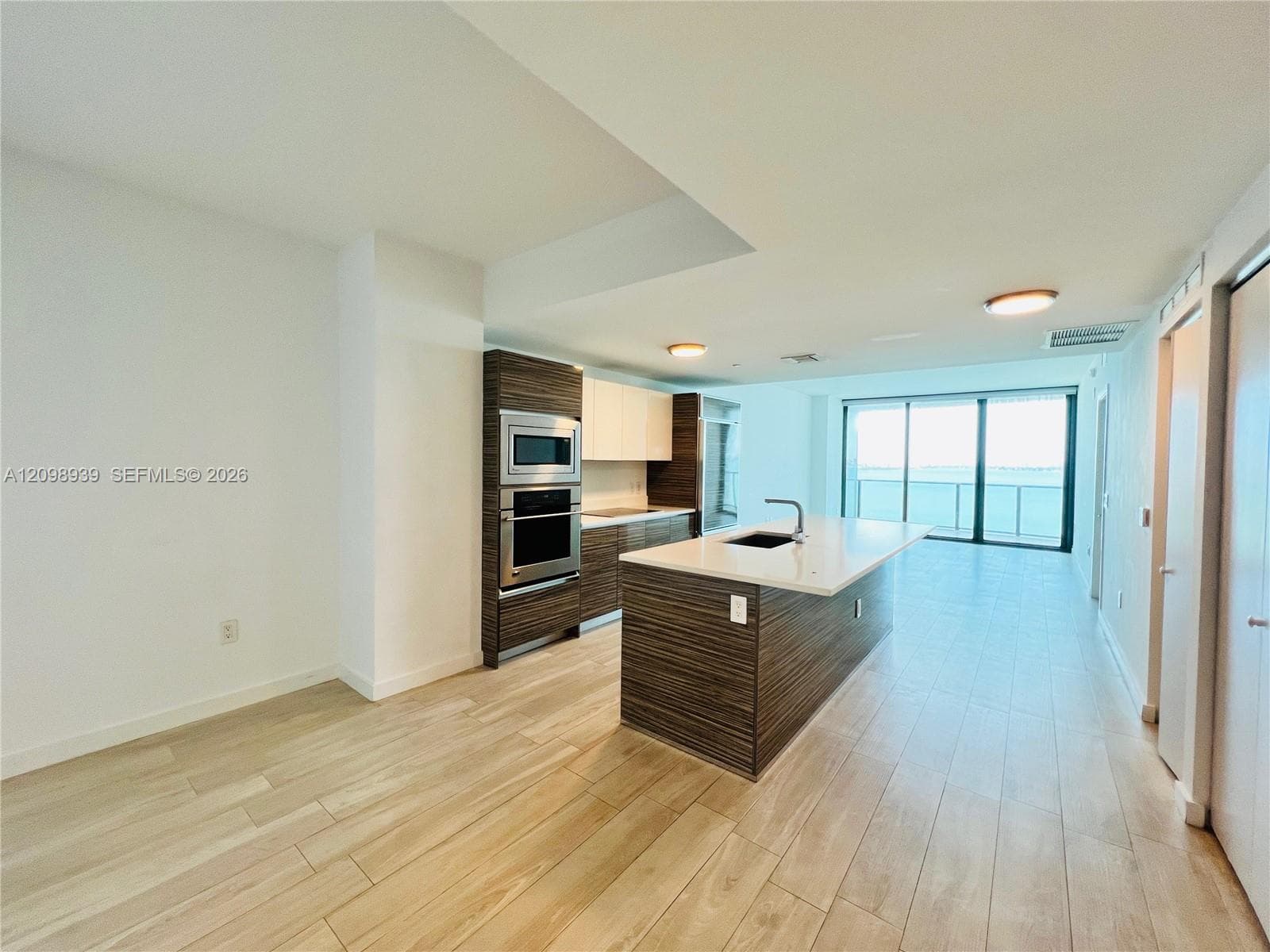 Open-concept kitchen with a large central island, stainless steel built-in appliances, and wood-finish cabinetry