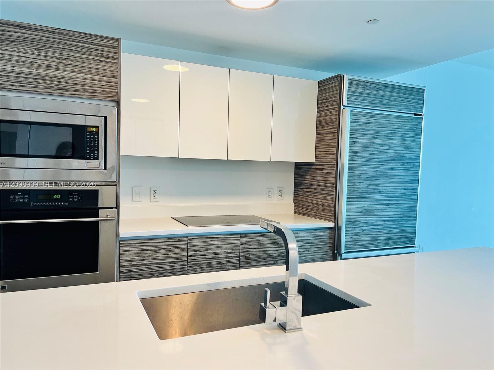 Modern kitchen featuring stainless steel appliances, light countertops, wood-finish cabinetry, and a sleek undermount sink with a pull-down faucet