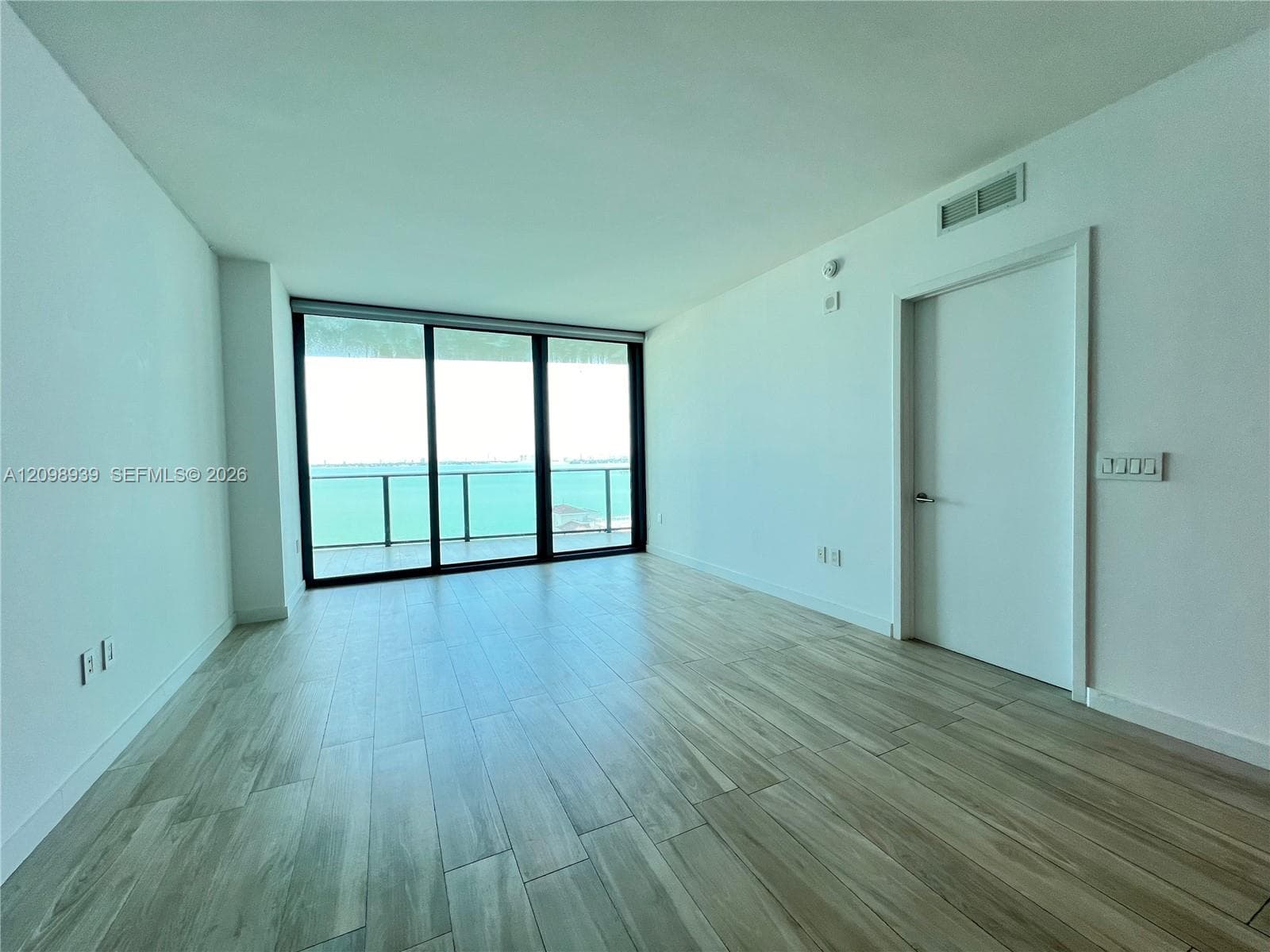 Expansive full-height glass doors, water scenery, wood-finish flooring, white walls, and a contemporary door