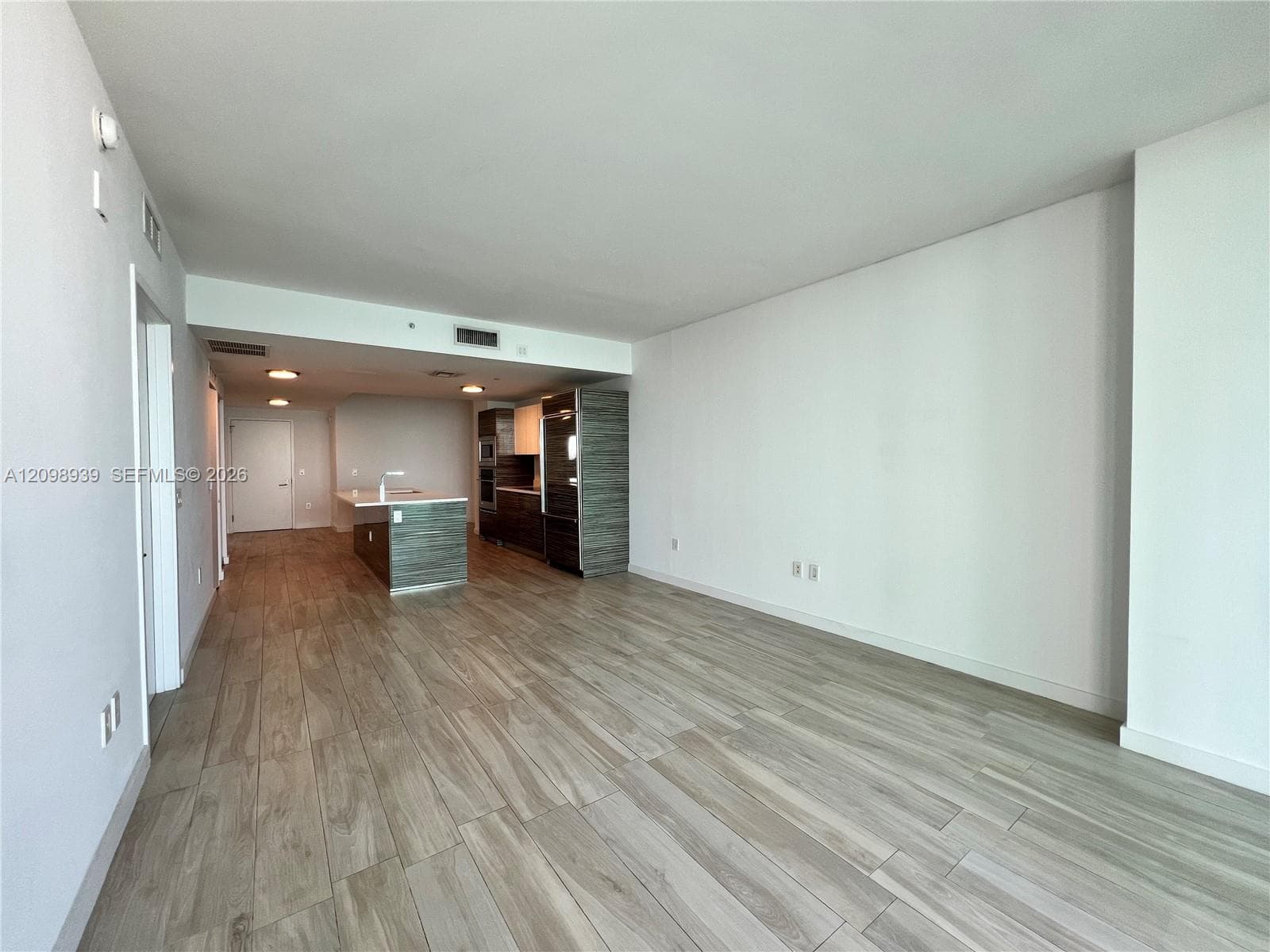 Open-concept living space featuring wood-look flooring, a kitchen island with a white countertop, and integrated stainless-steel appliances