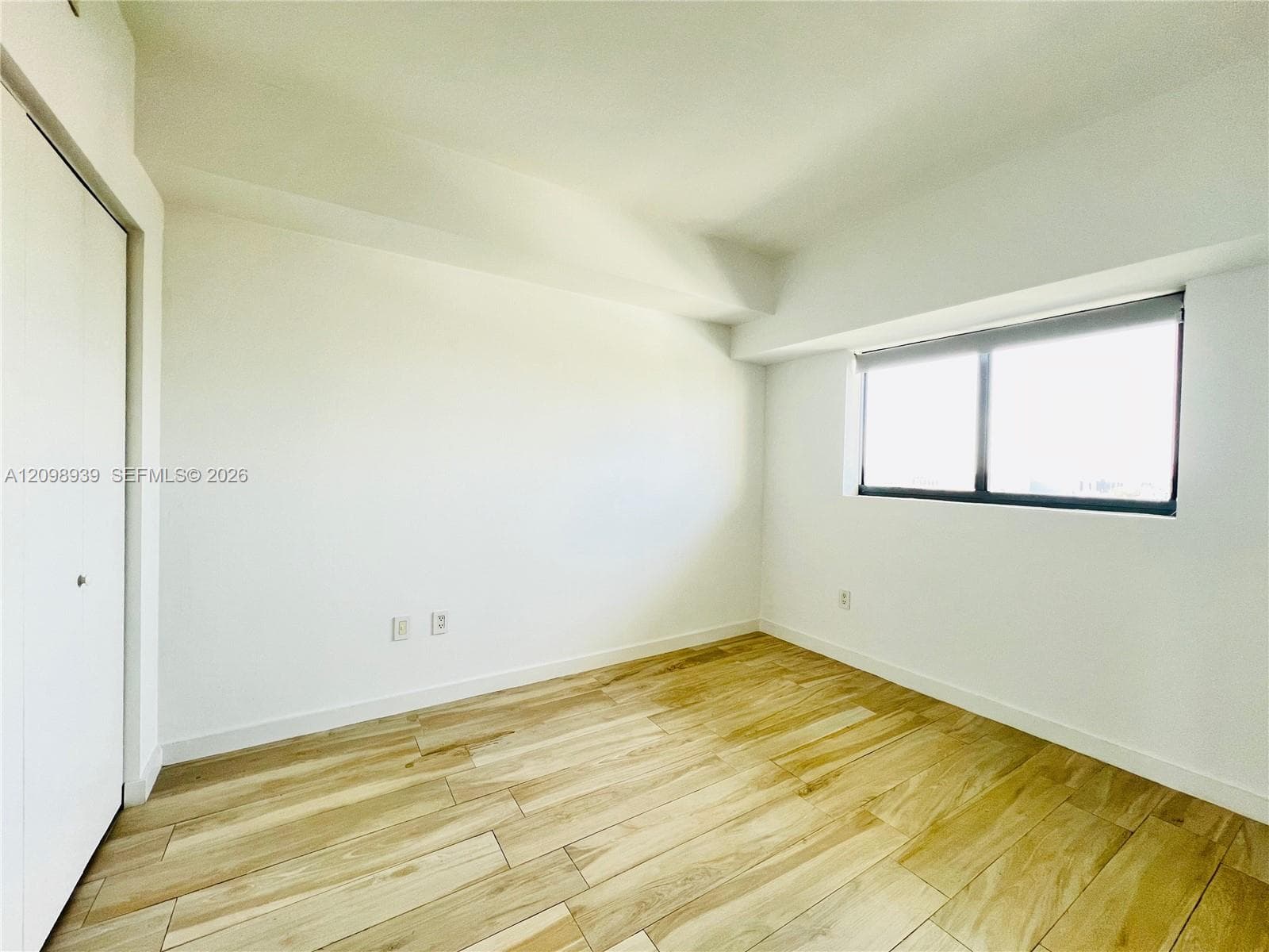 Wood-finish flooring with a light tone, white walls, and a window with a roller shade
