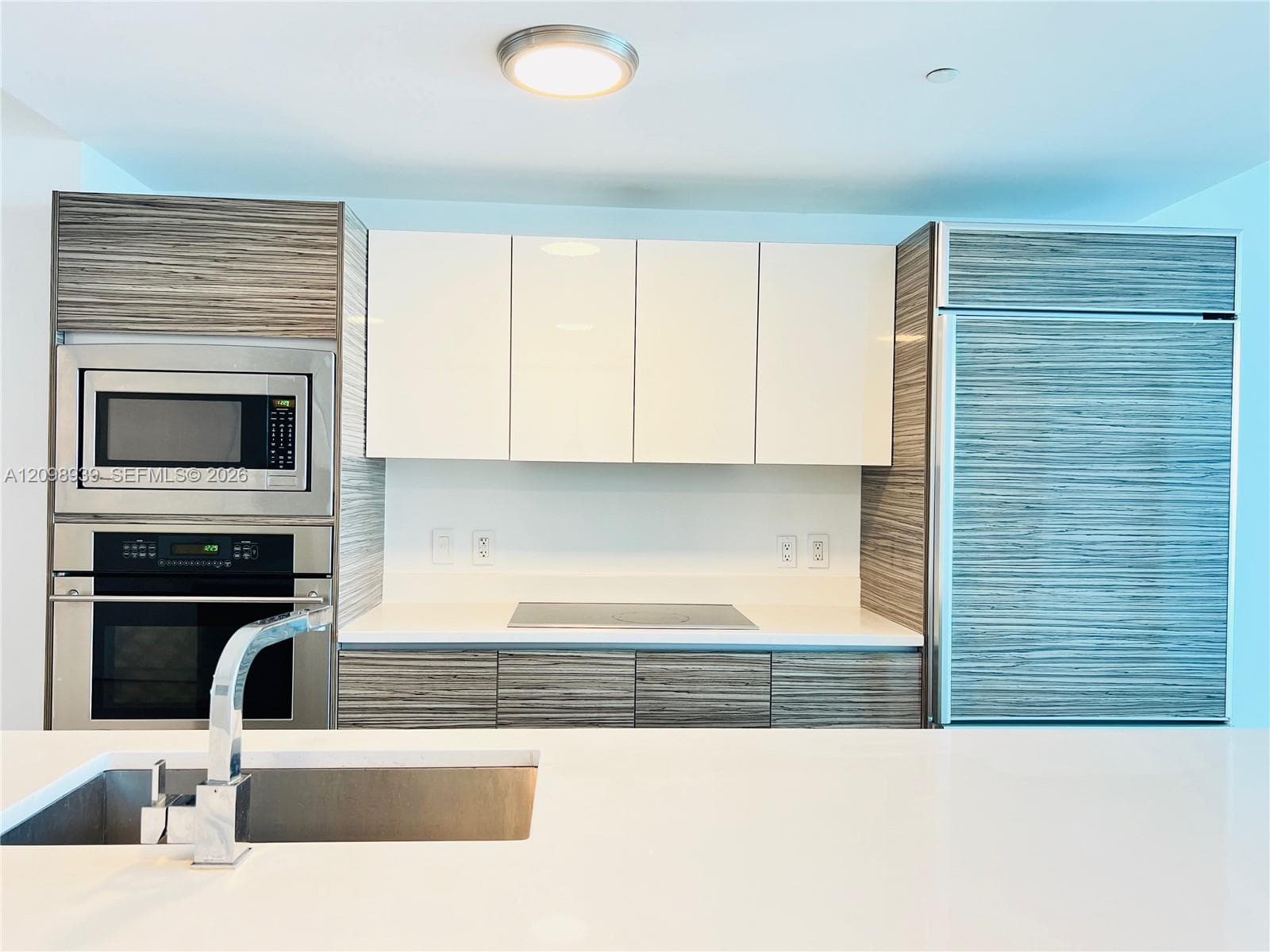 Modern kitchen featuring integrated appliances, white upper cabinetry, wood-finish lower cabinetry, and a stainless steel sink with a contemporary faucet
