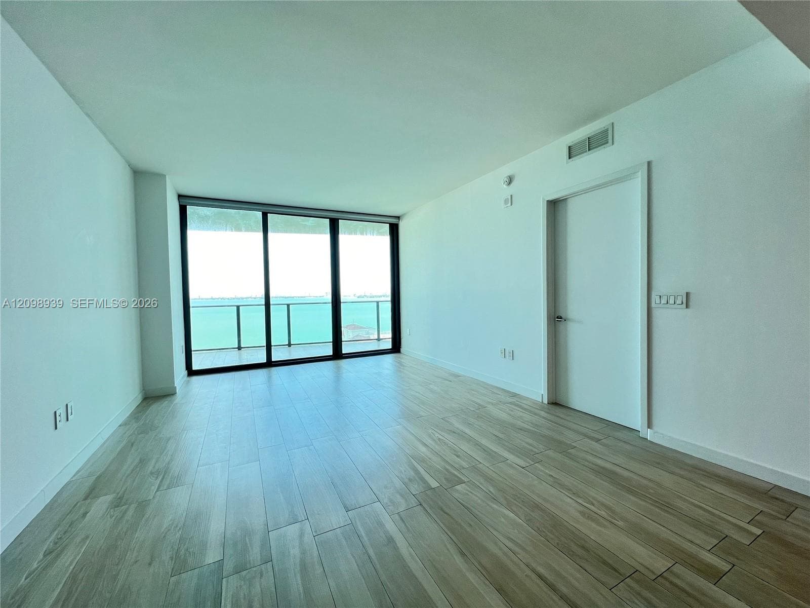 Spacious room featuring wood-finish flooring, a wall of sliding glass doors, and a balcony with glass railings