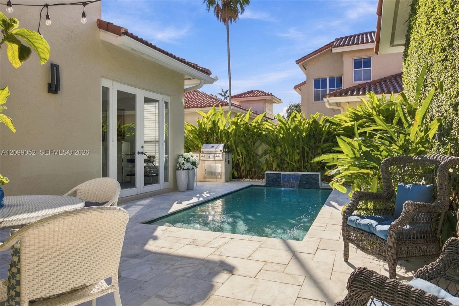 Outdoor living space featuring a tiled patio, private swimming pool with a stone-accented water feature, built-in stainless steel grill, and manicured perimeter landscaping