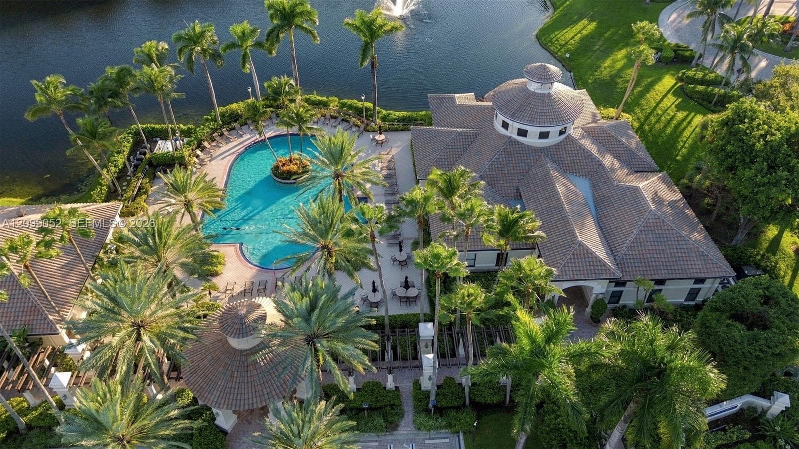 Aerial perspective featuring a clubhouse with a tiled hip roof, a paved pool deck, a swimming pool with a central island, a detached gazebo, and extensive landscaping
