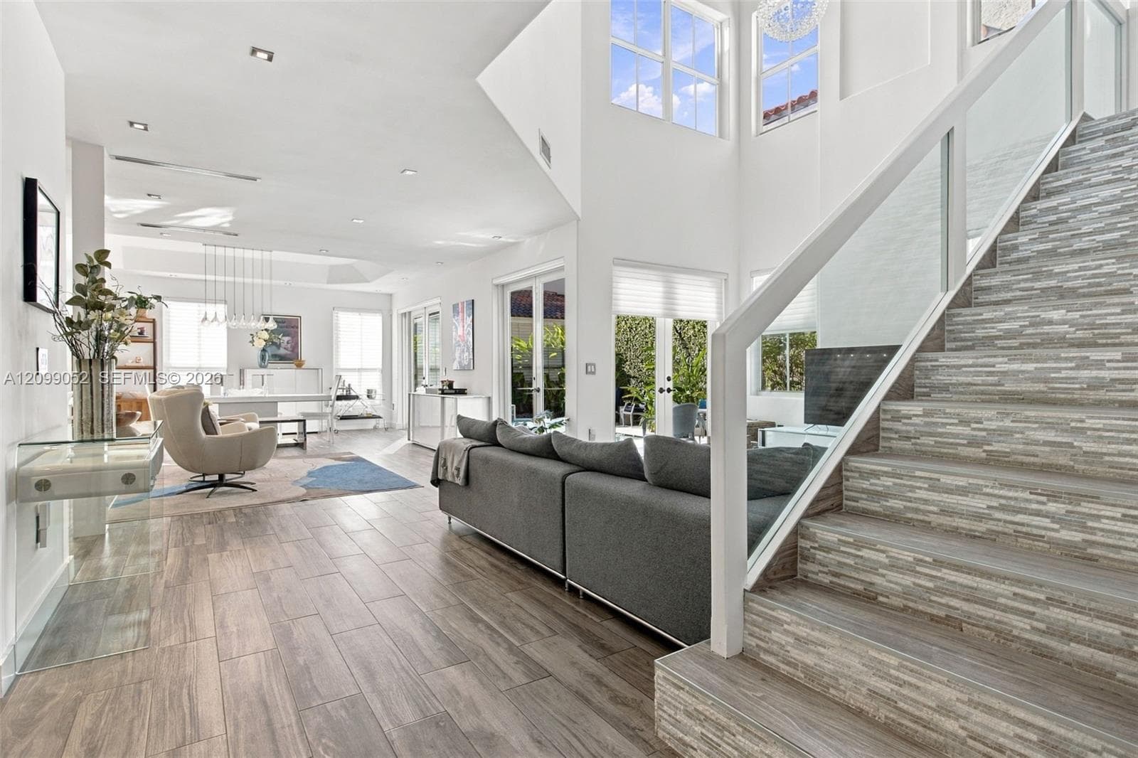 Double-height ceiling, glass-paneled staircase railing, stacked stone-texture stair risers, wood-finish flooring, and multiple sets of French doors