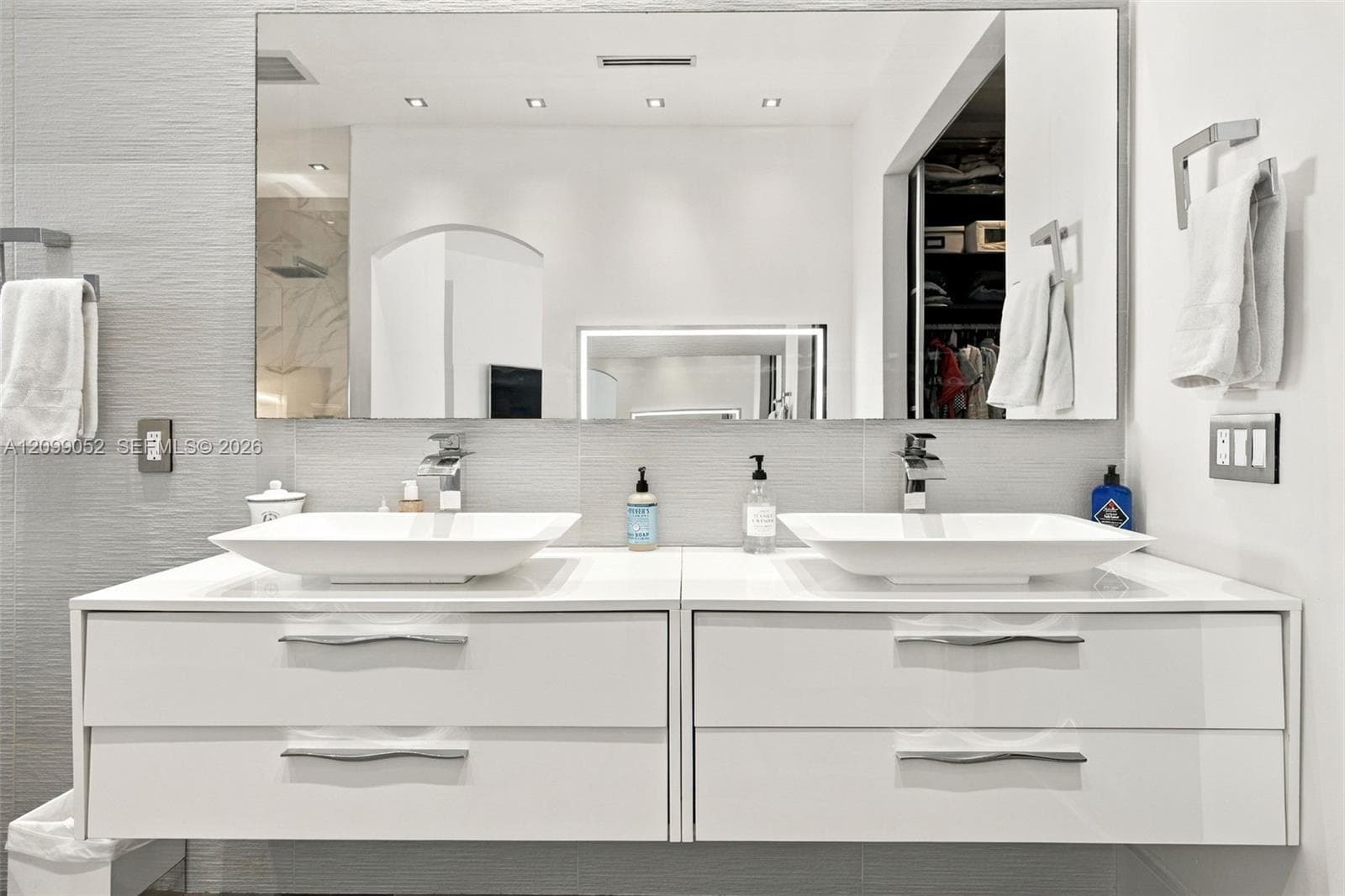 Floating dual vanity featuring white cabinetry, rectangular vessel sinks, chrome faucets, and large wall-mounted mirror with recessed lighting