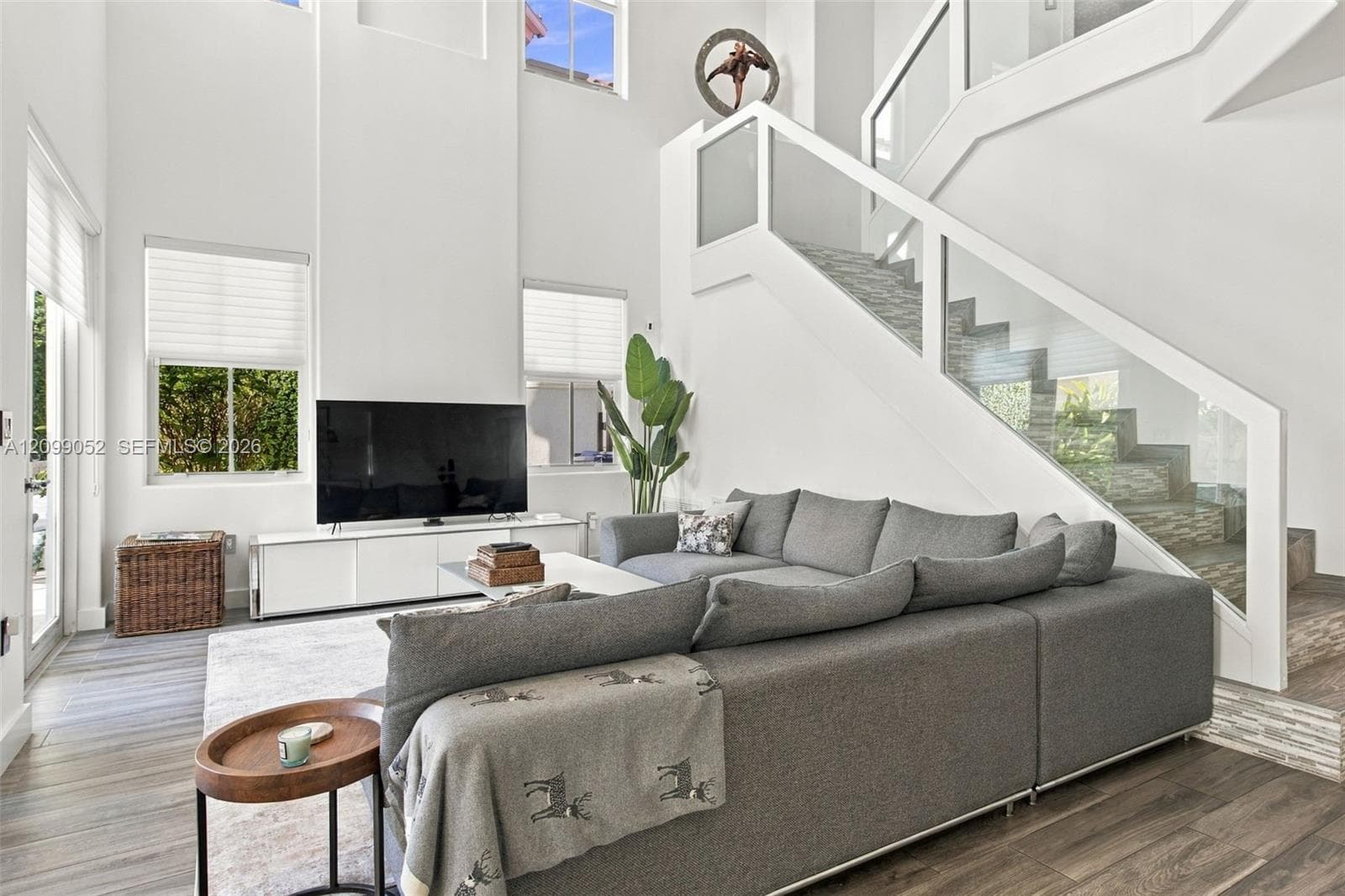 Double-height ceiling, glass-paneled staircase railing, wood-finish flooring, and expansive windows
